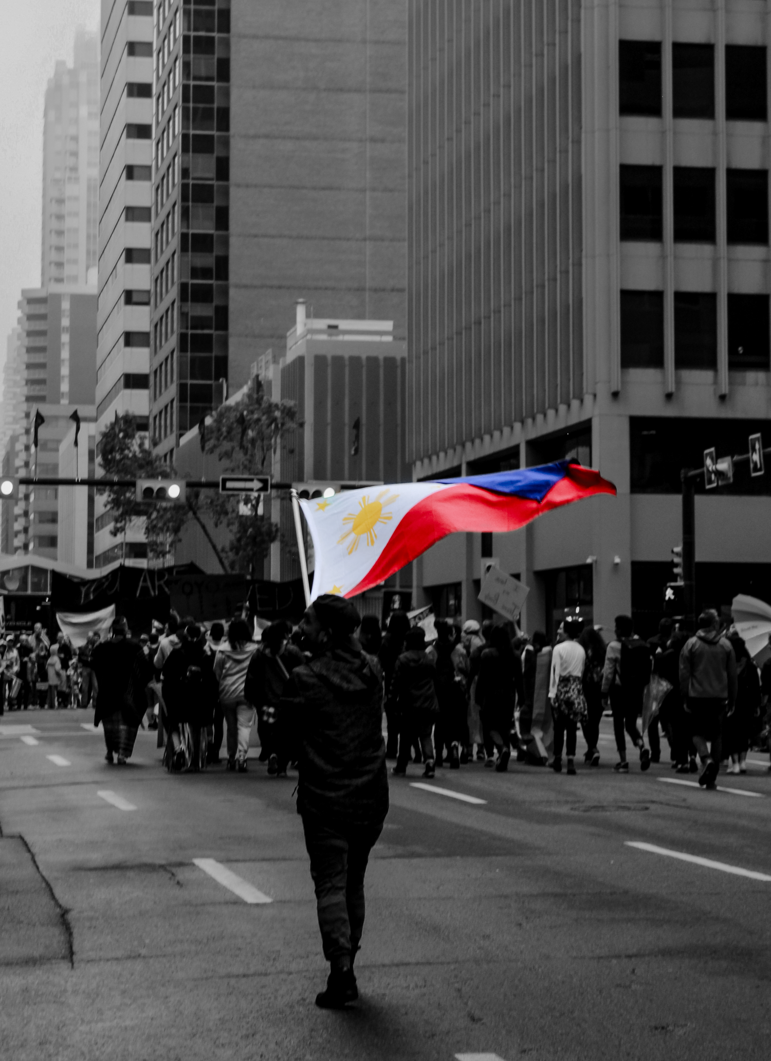 Black and white street protest scene with Philippine flags waving among crowd of demonstrators.