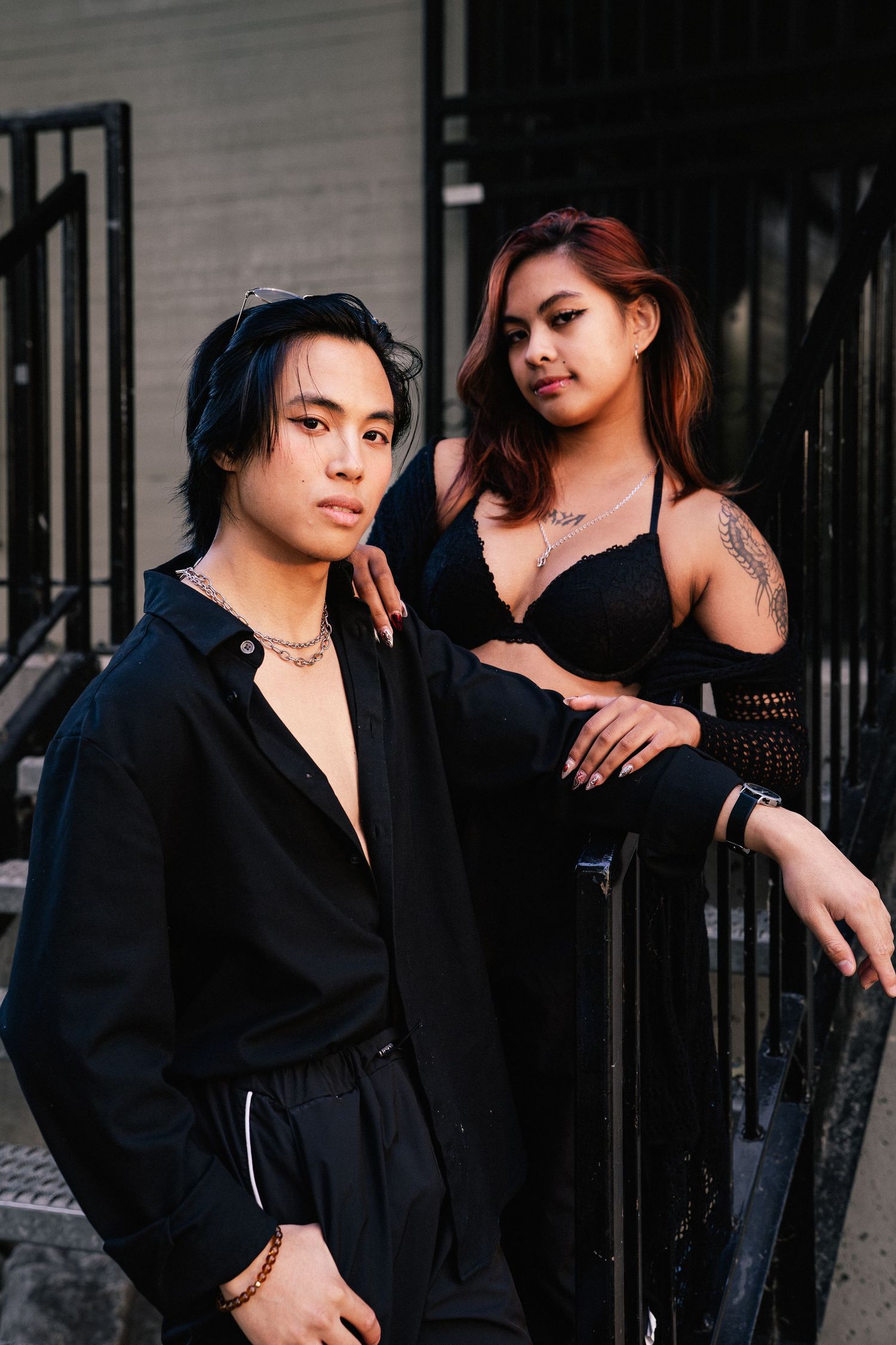Edgy fashion portrait of two models in black outfits against urban backdrop.