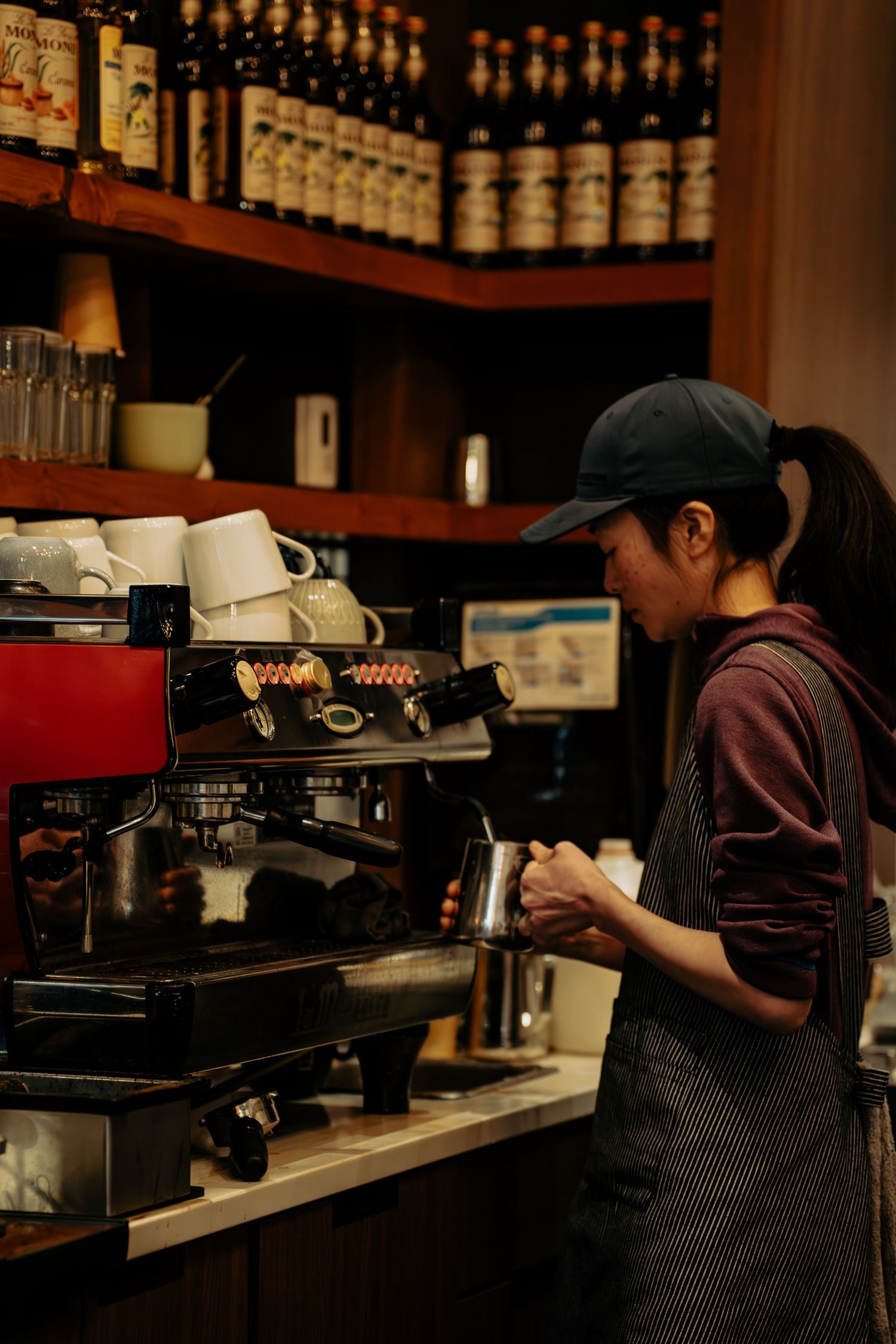 Dark coffee shop interior with espresso machines and bottles lined up on wooden shelves.