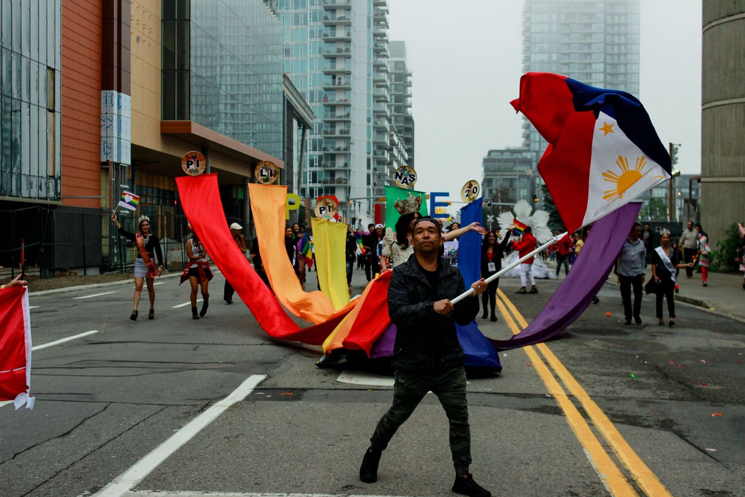 Person waving Philippine flag with rainbow fabric display on city street.
