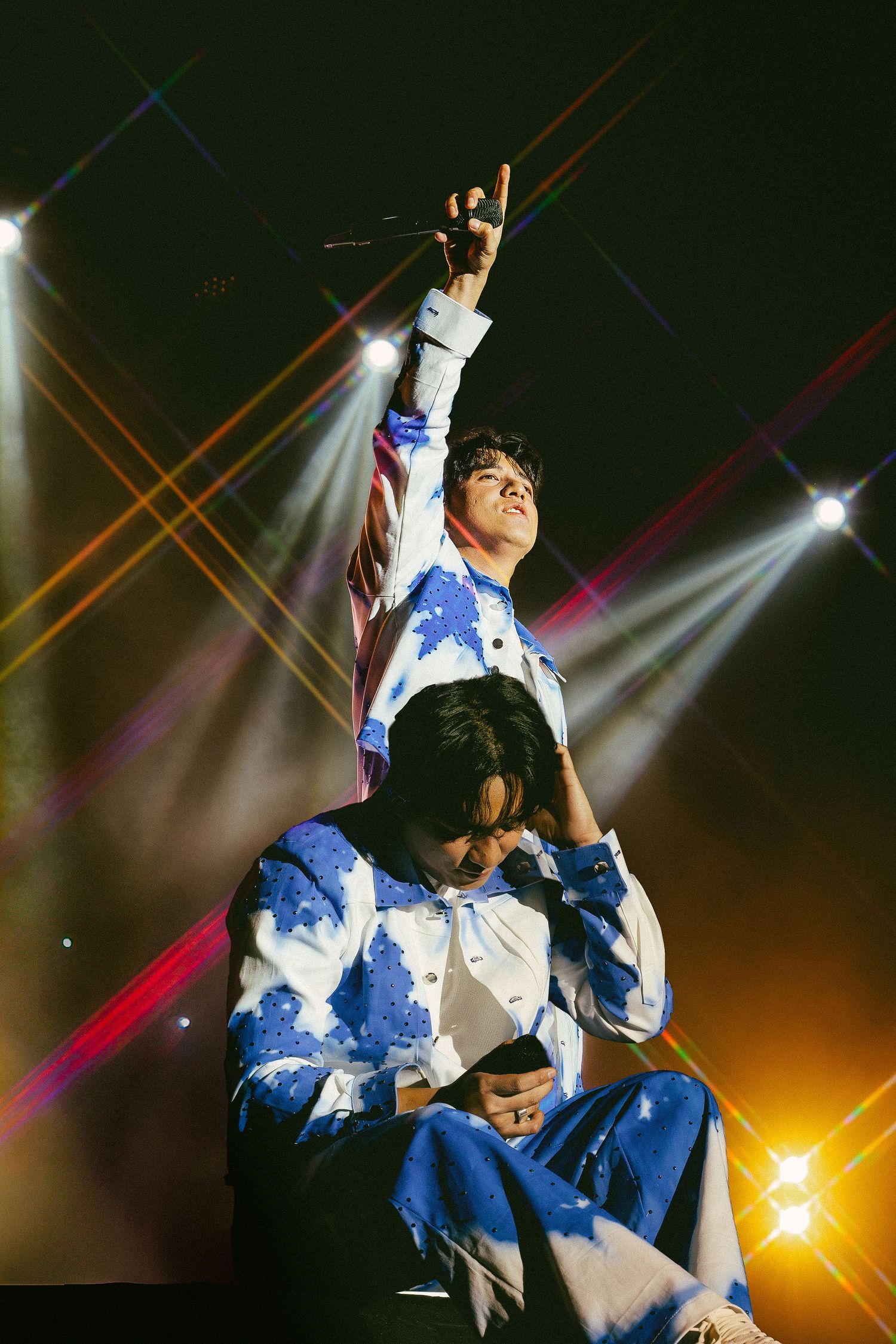 Two performers in matching blue and white outfits on stage with colorful laser lights during a concert.