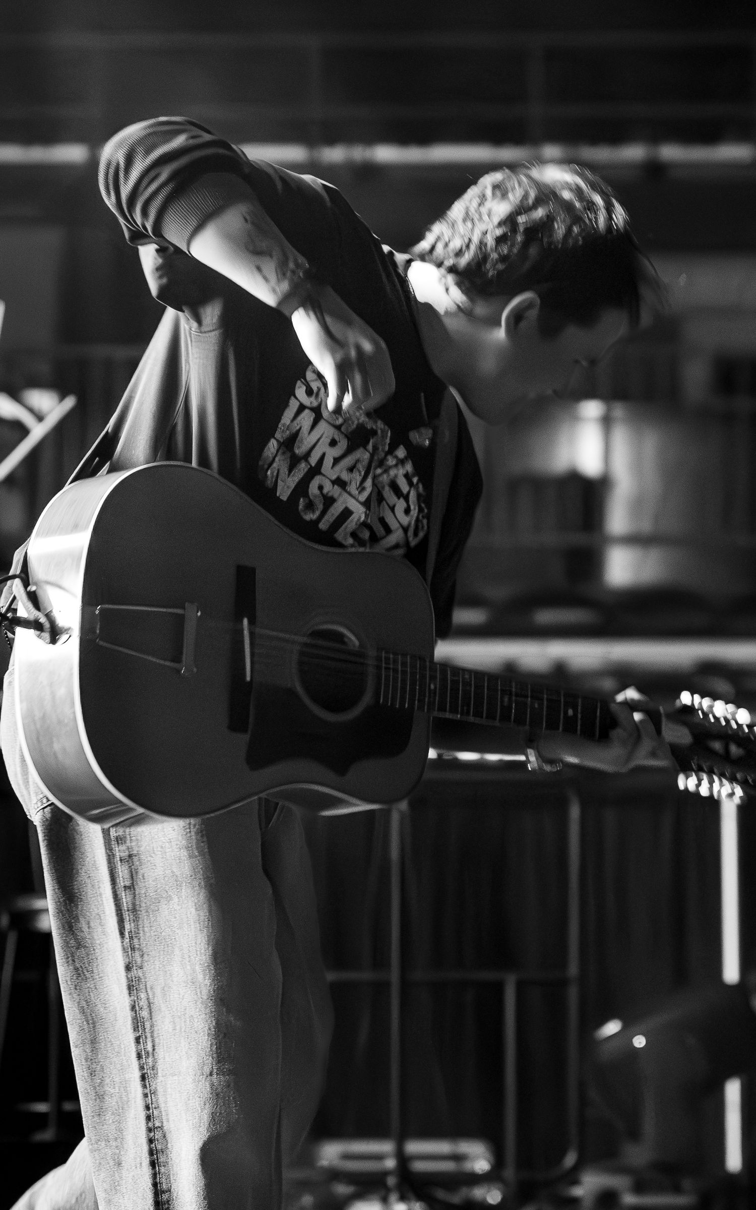 Black and white close-up shot of a musician playing acoustic guitar on stage.