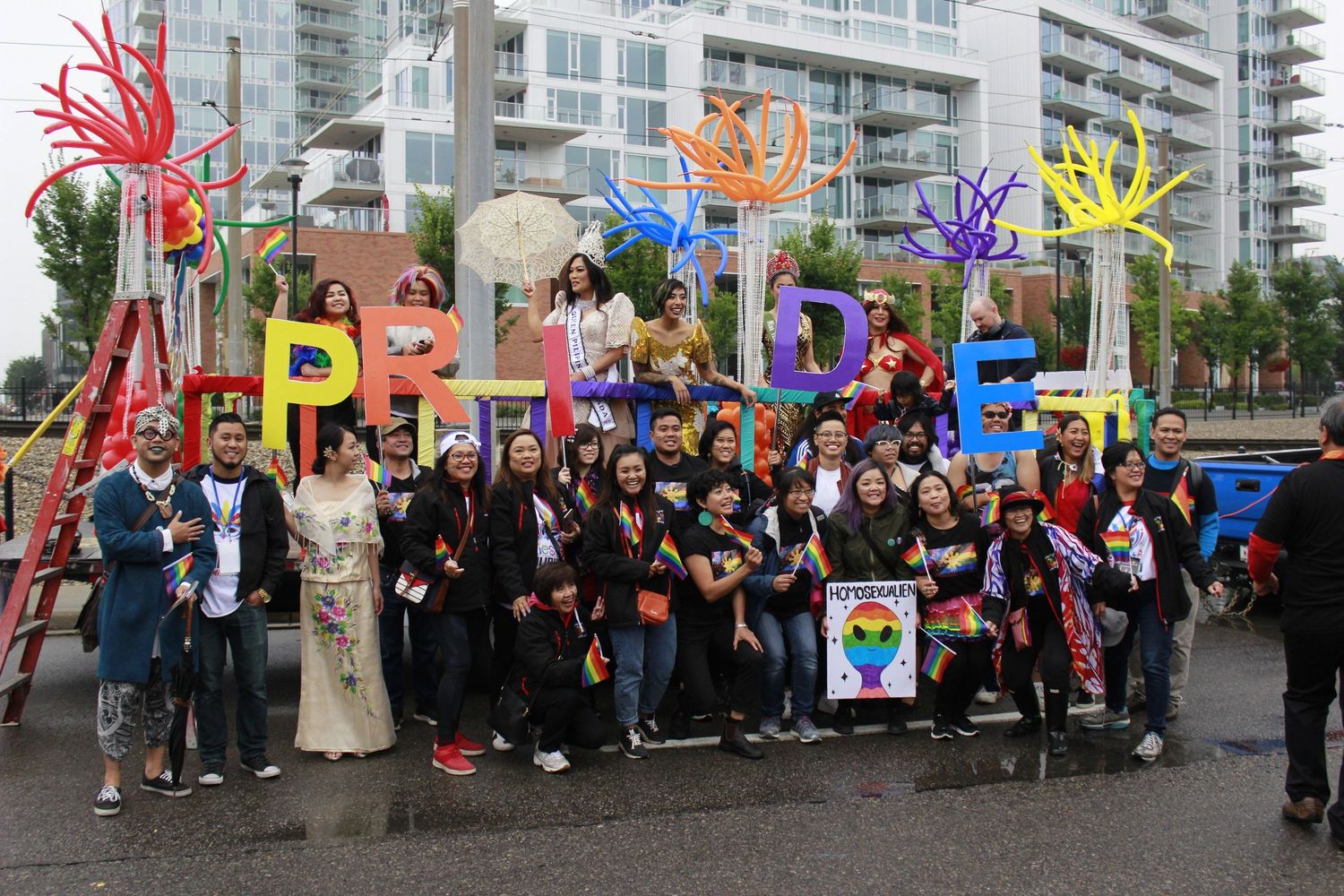 Large group gathered outdoors with colorful art displays and banners.