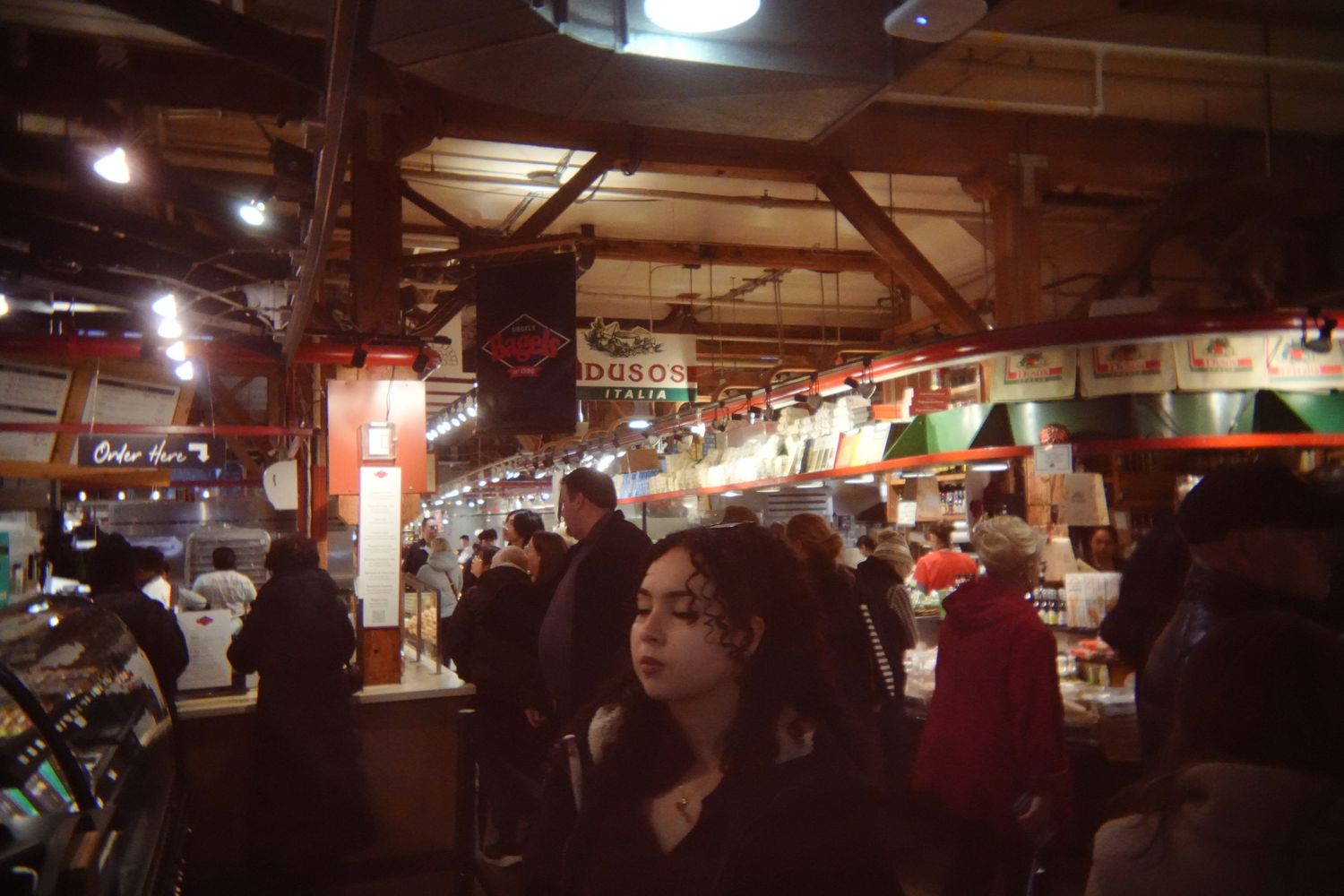 Dimly lit indoor market hall with red ambient lighting and people browsing vendor stalls.