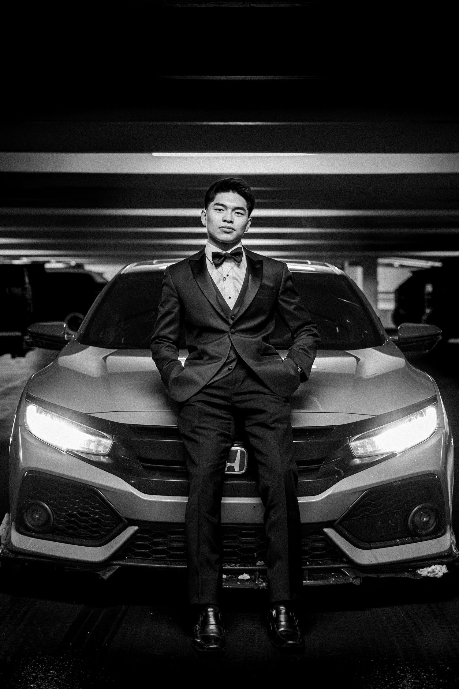 Dramatic black and white photos of a luxury car with headlights illuminated in a dark parking garage.