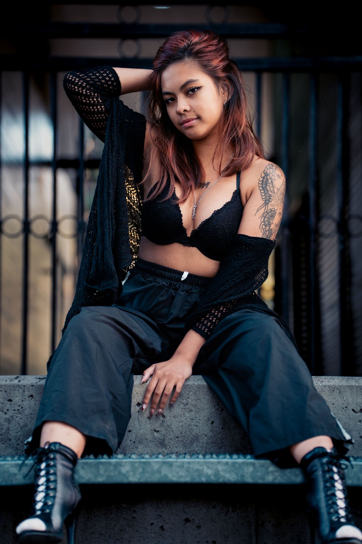 Fashion portrait of a model in black outfit with combat boots sitting on concrete steps.
