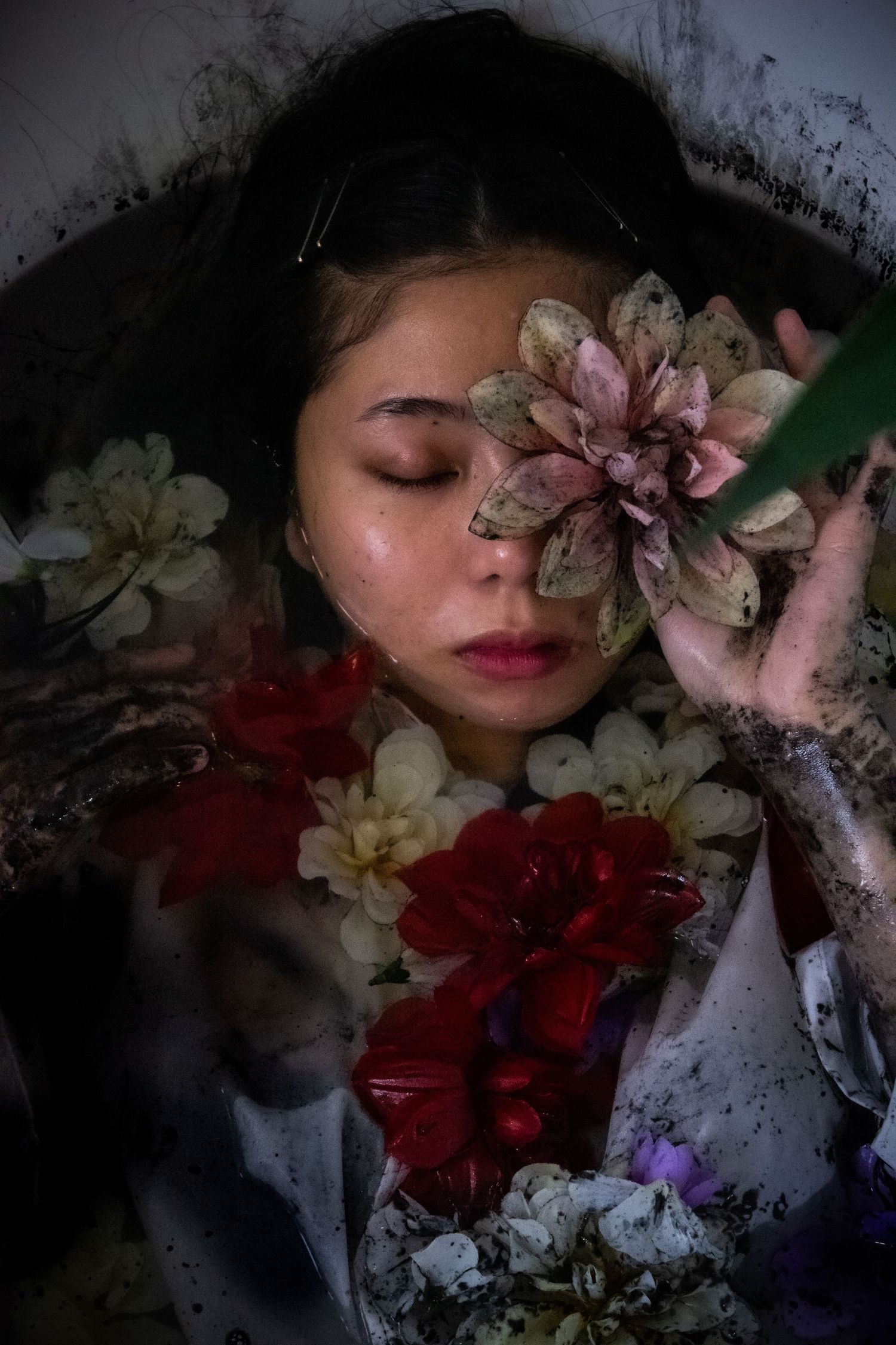 Artistic dark portrait with delicate pink and white flowers creating a dreamy ethereal mood.
