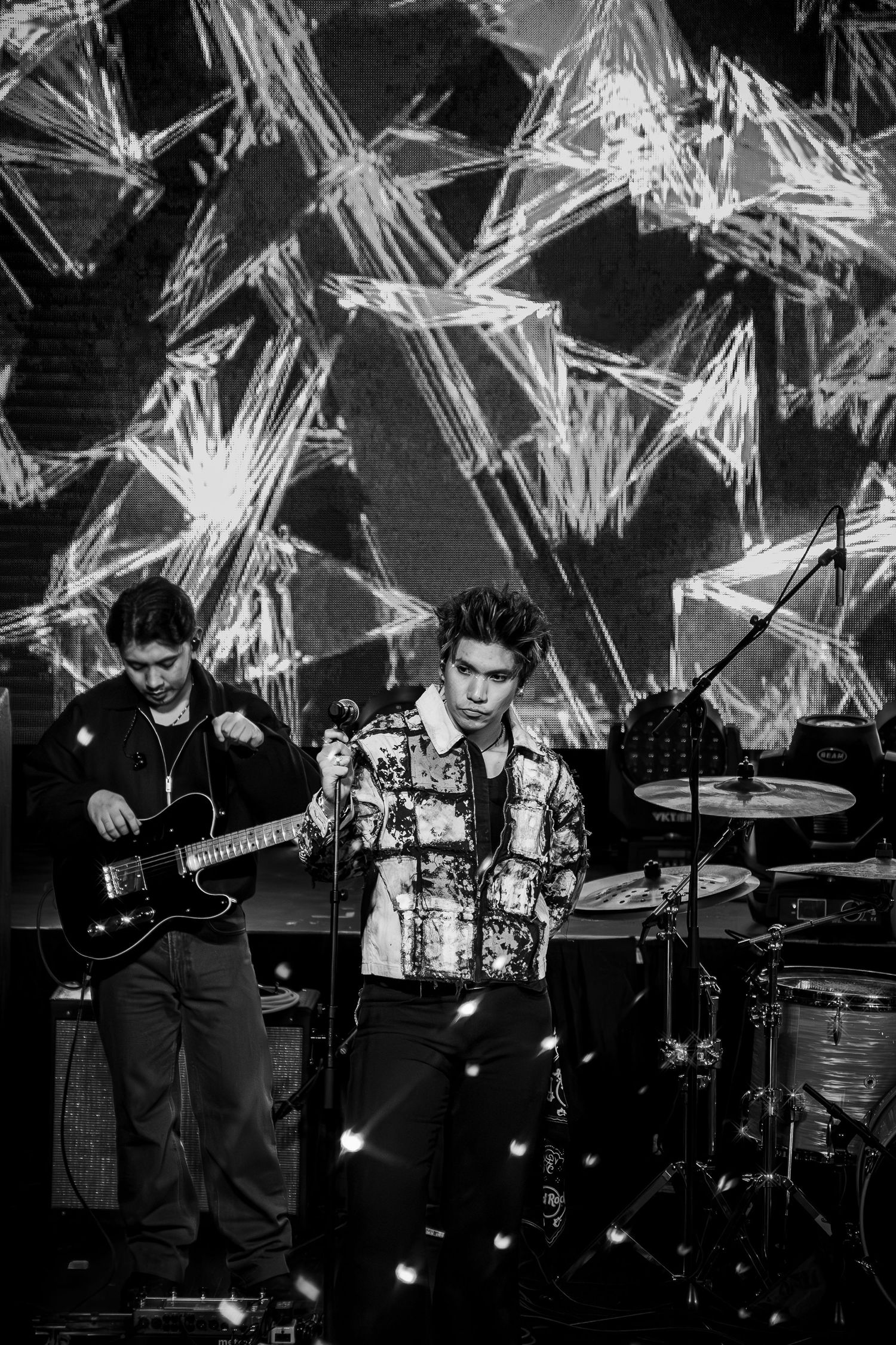 Band performing on stage with geometric light display backdrop.