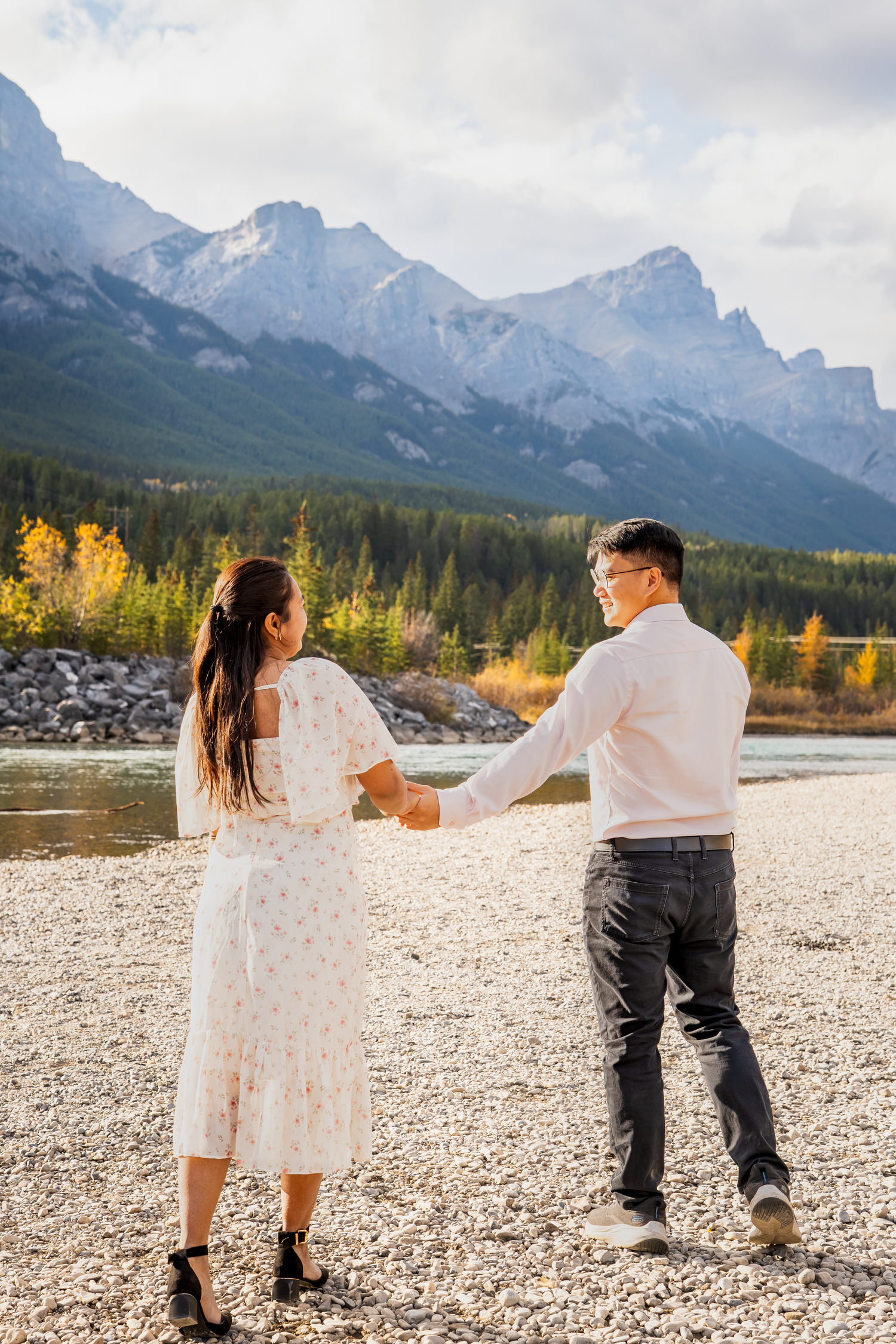 A couple dances and plays on a rocky beach with mountain views in the background.