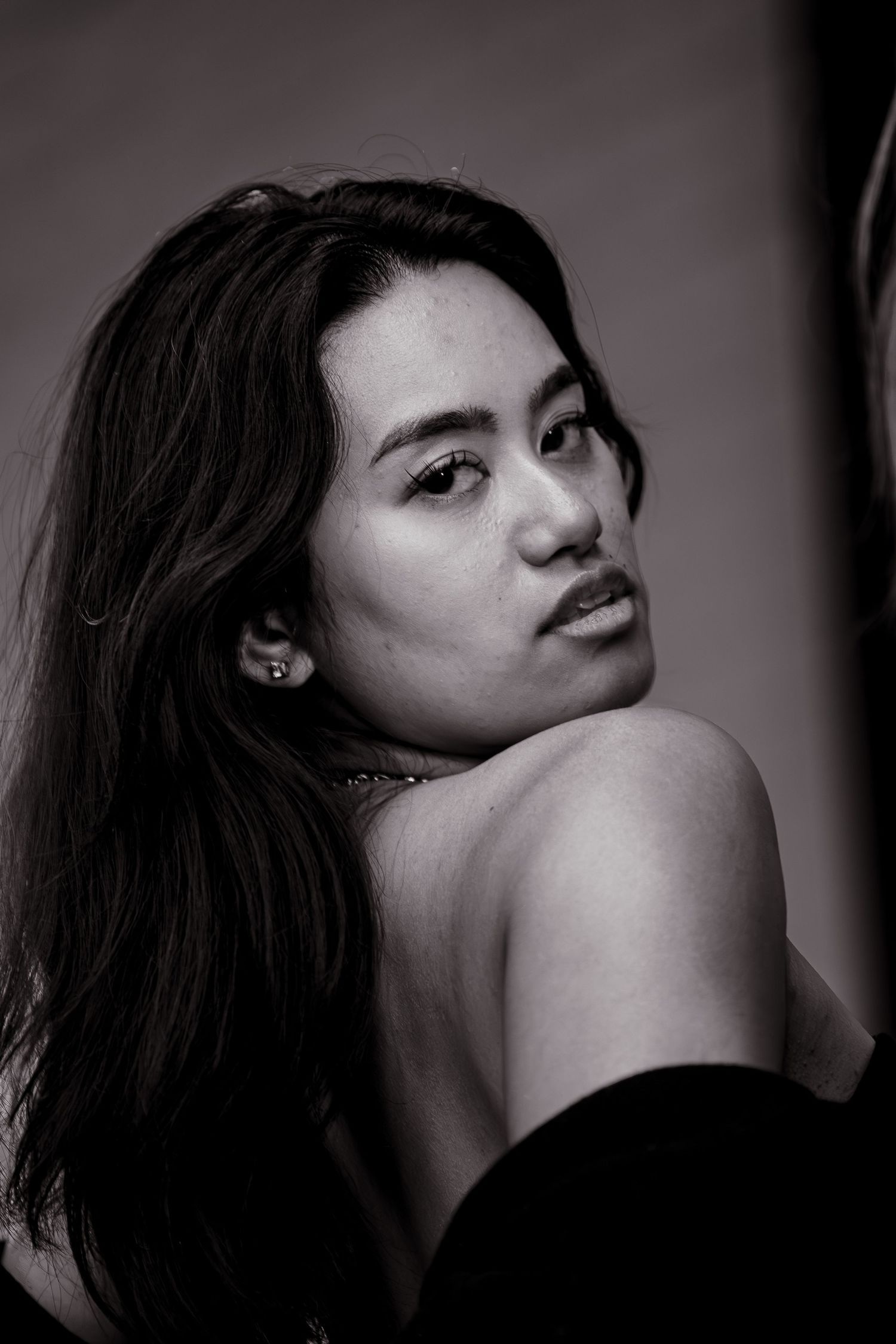 Artistic black and white portrait showcasing dramatic lighting and shoulder pose.