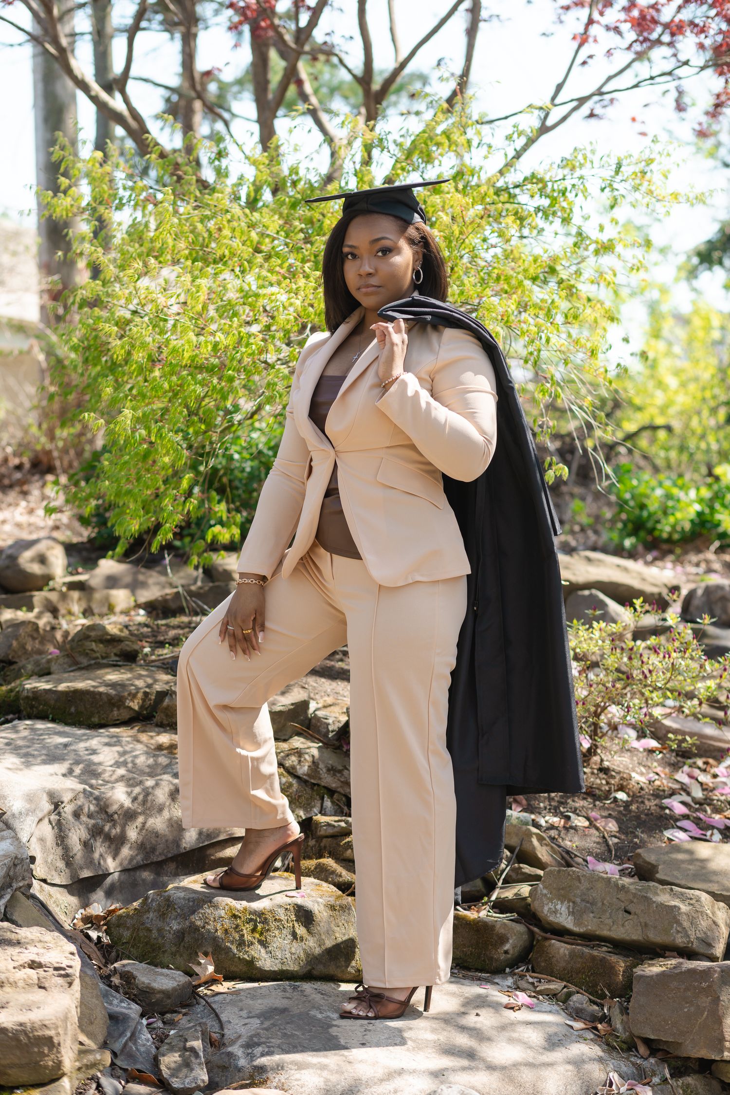 Maternity photoshoot on rocky terrain with woman in beige outfit and black jacket.