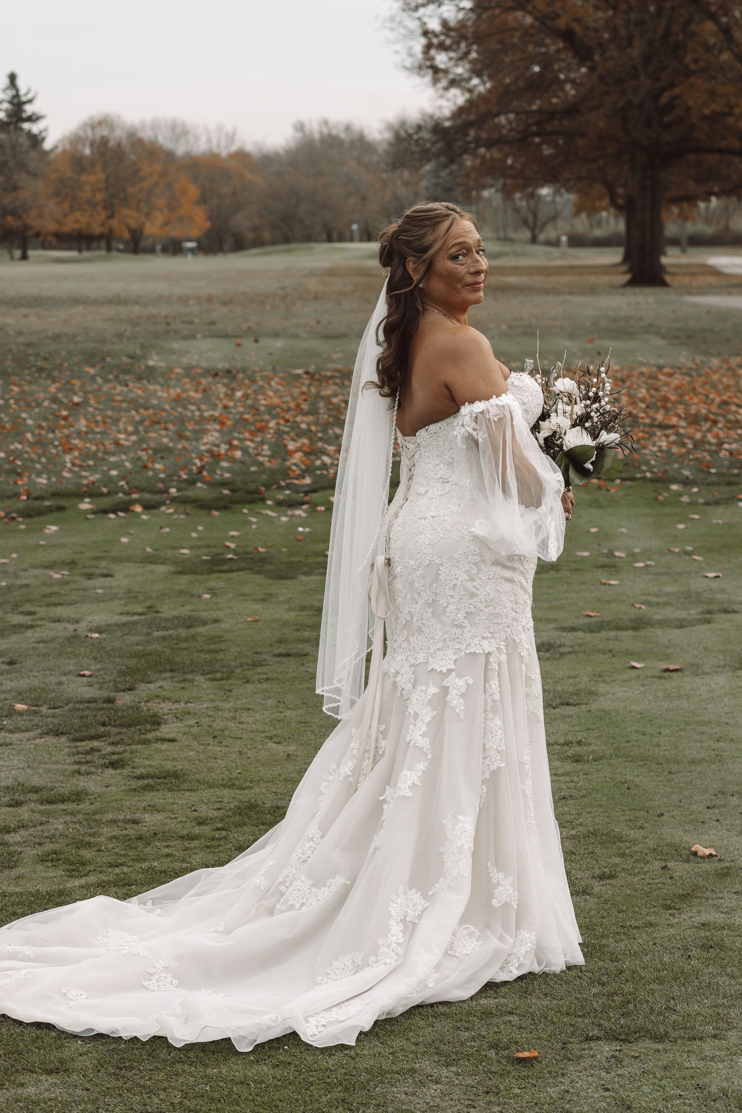 Elegant wedding dress with lace details photographed in autumn setting.