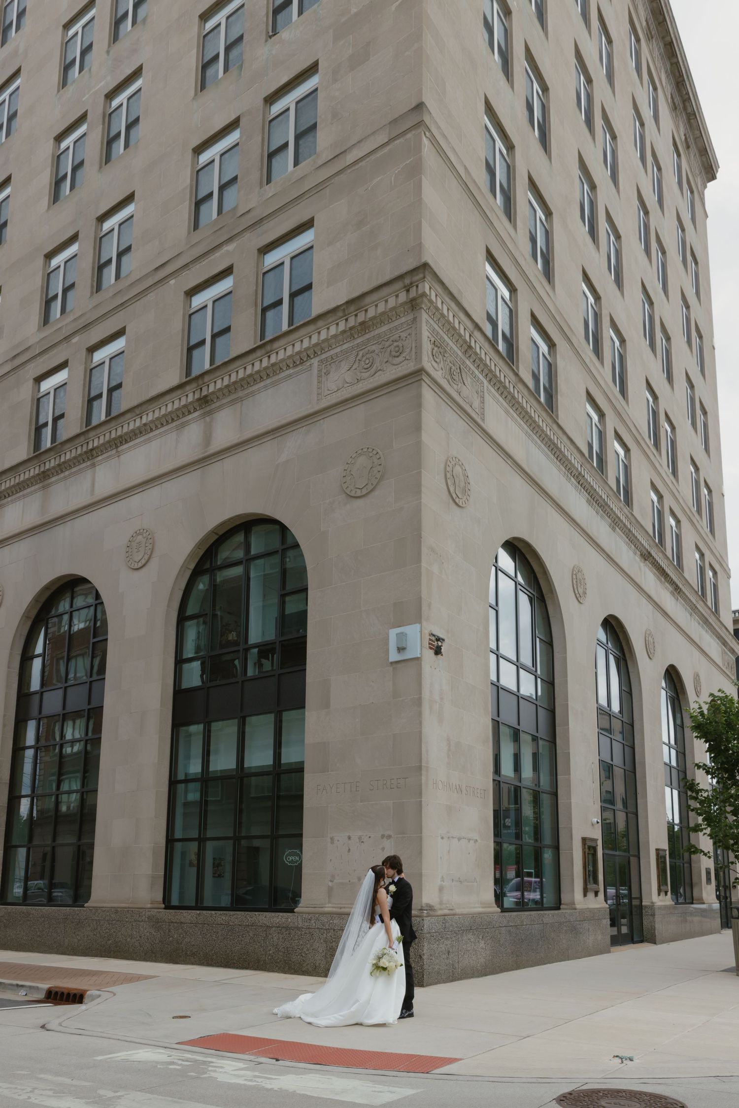 Bride and groom sharing a kiss outside a classic stone building on their wedding day.