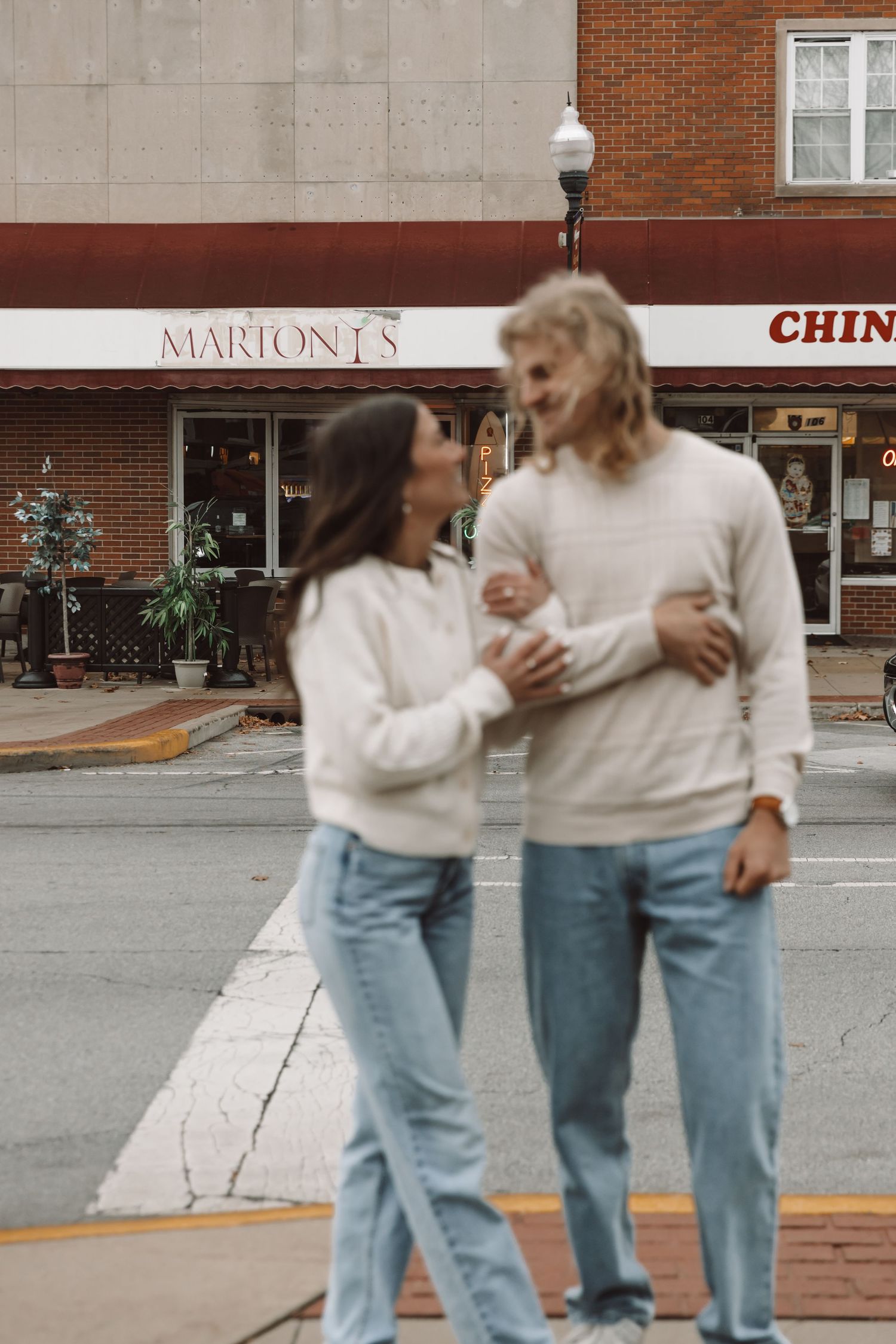 Two people in matching white sweaters and jeans walking together on city street.