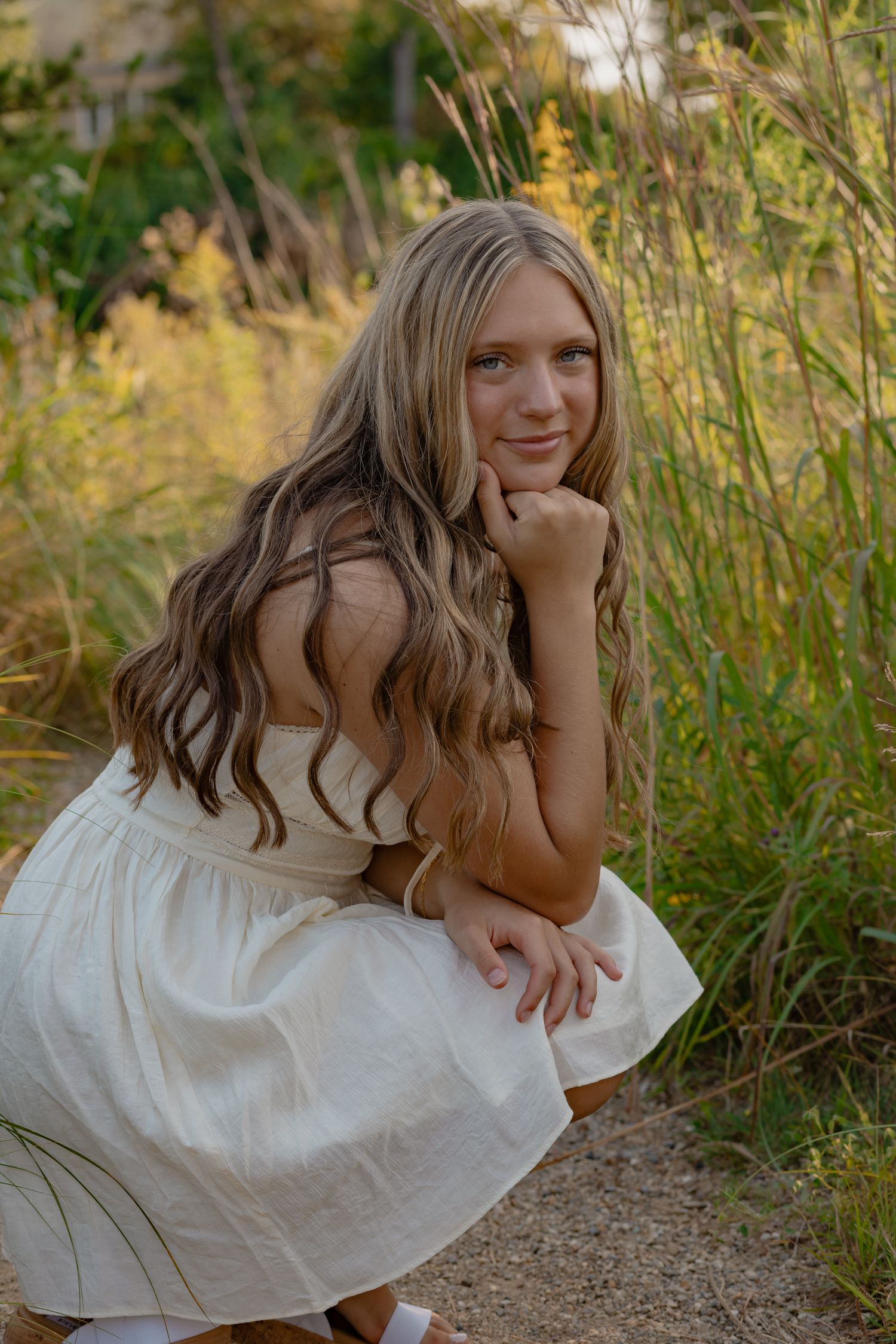 Woman in white dress poses playfully in tall summer grass.