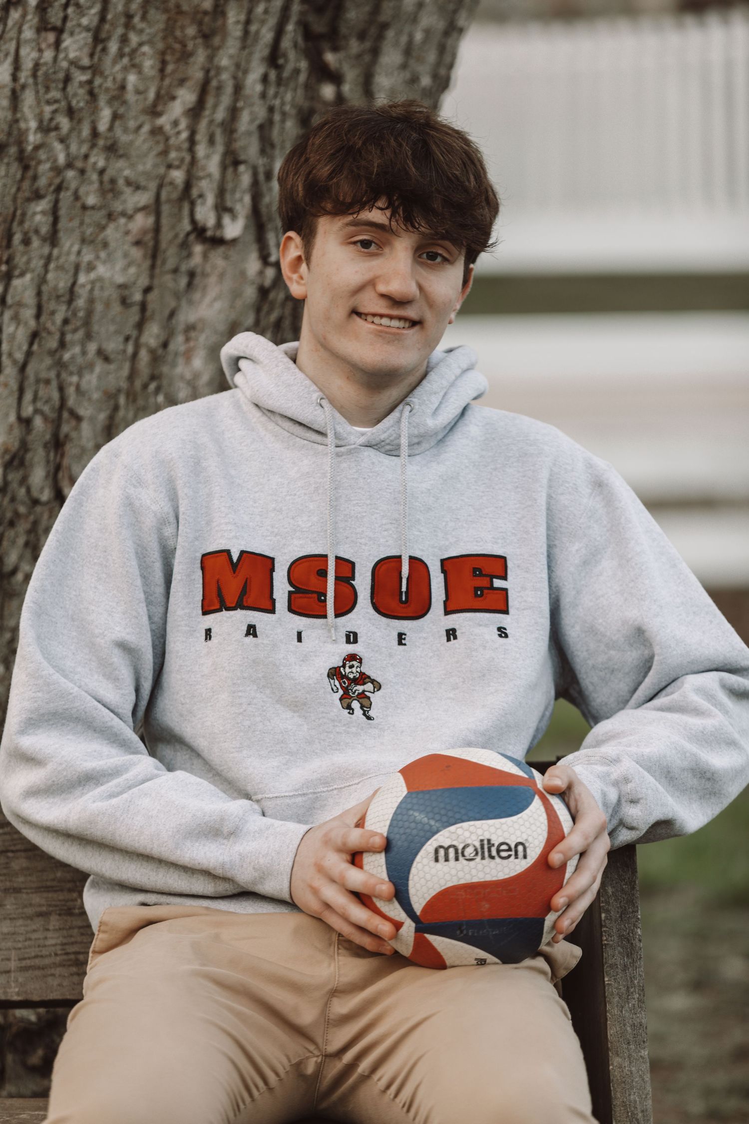 Someone wearing a grey MSOE hoodie holds a basketball while sitting on wooden steps.