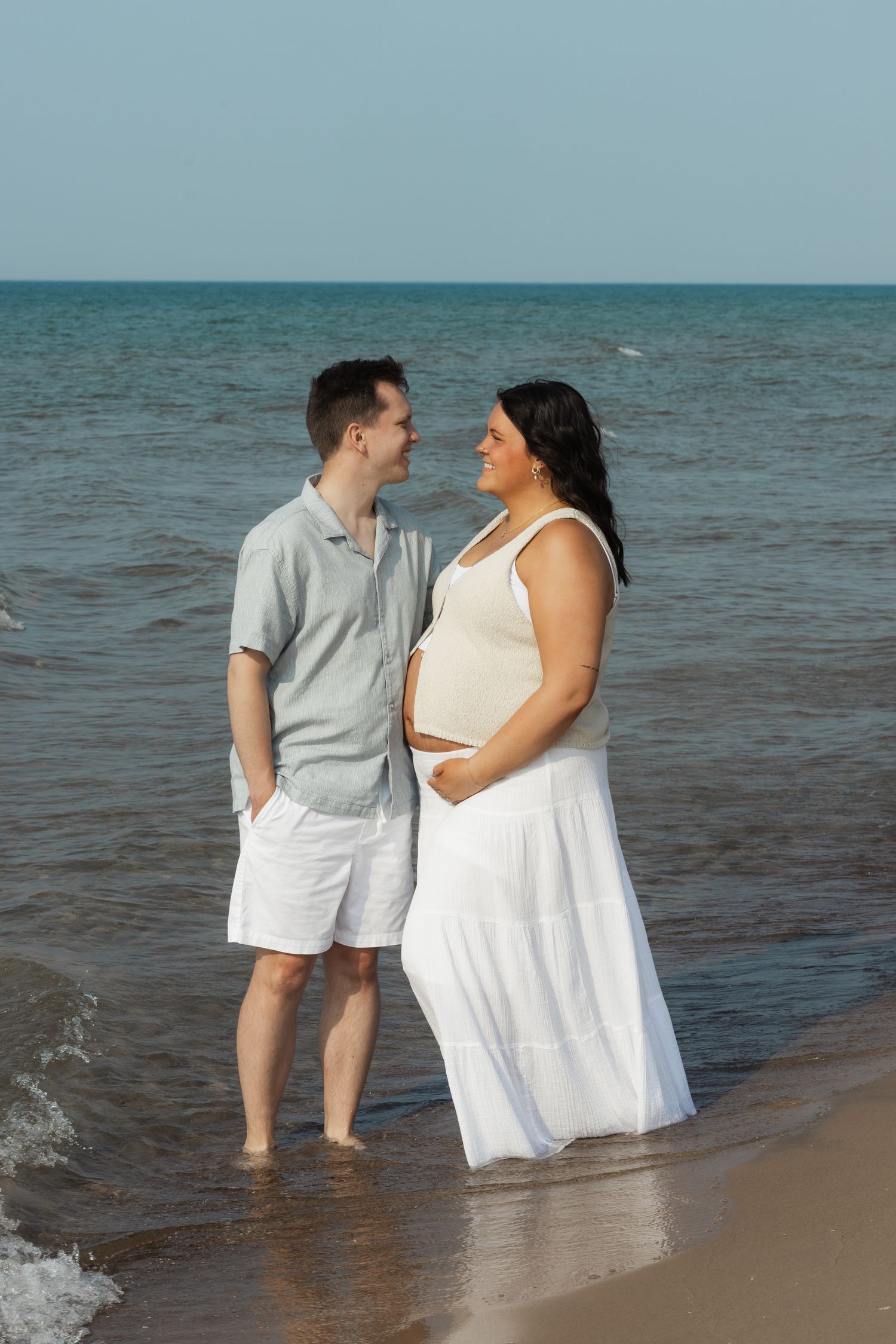 Couple standing together at the beach edge in white summer outfits.