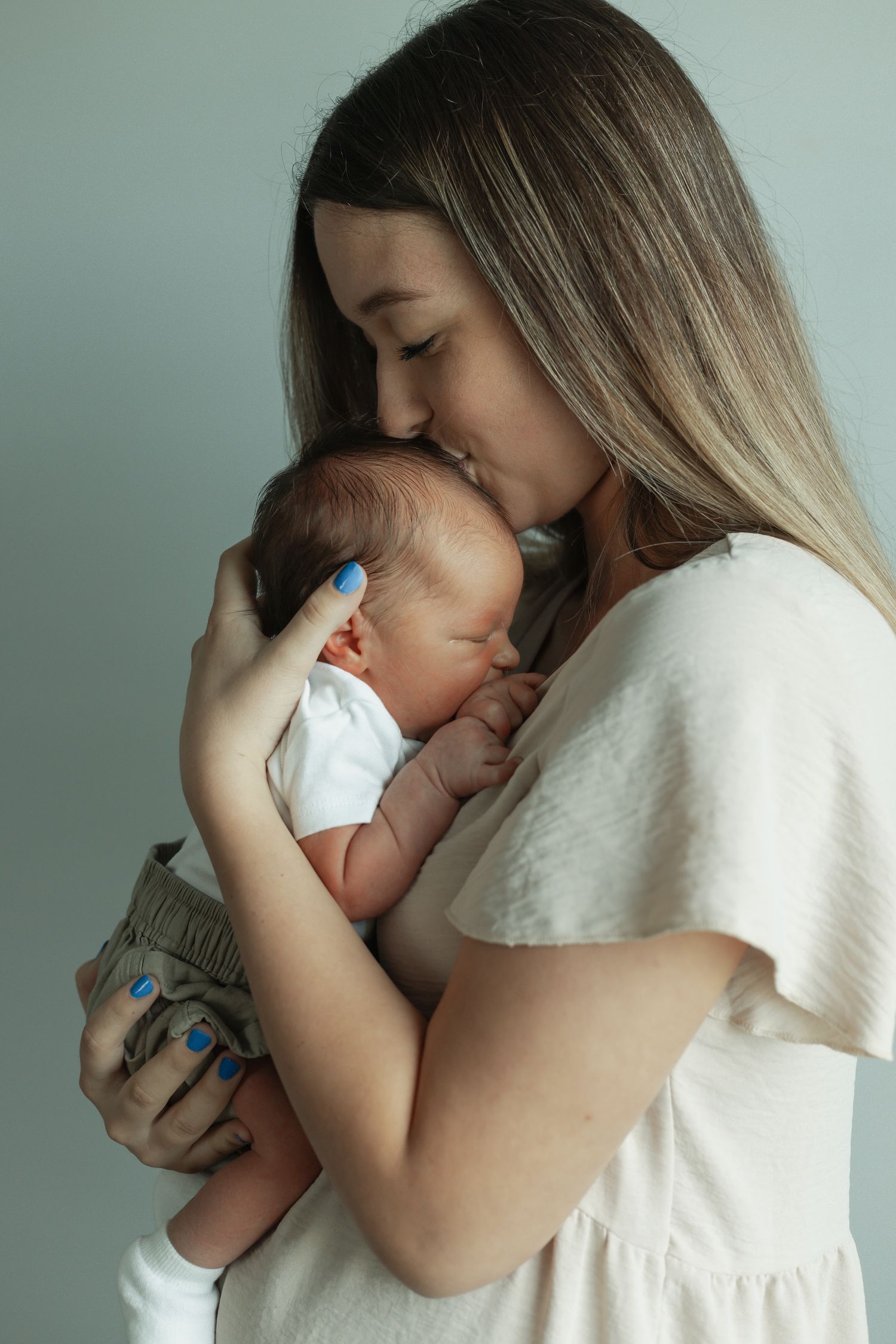 Tender moment between parent and baby in soft white lighting against neutral background.