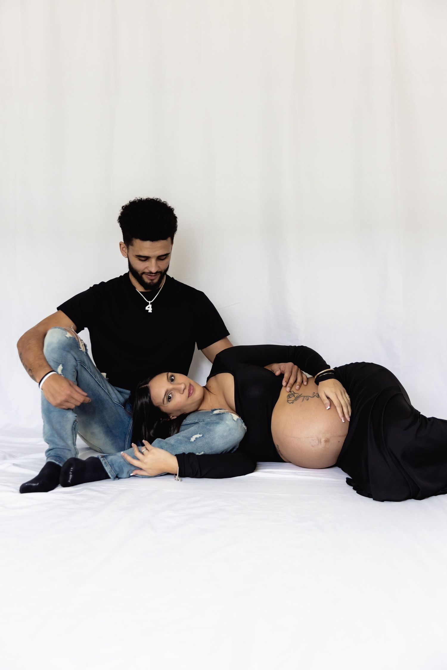 Maternity photo session with couple in black outfits on white background.