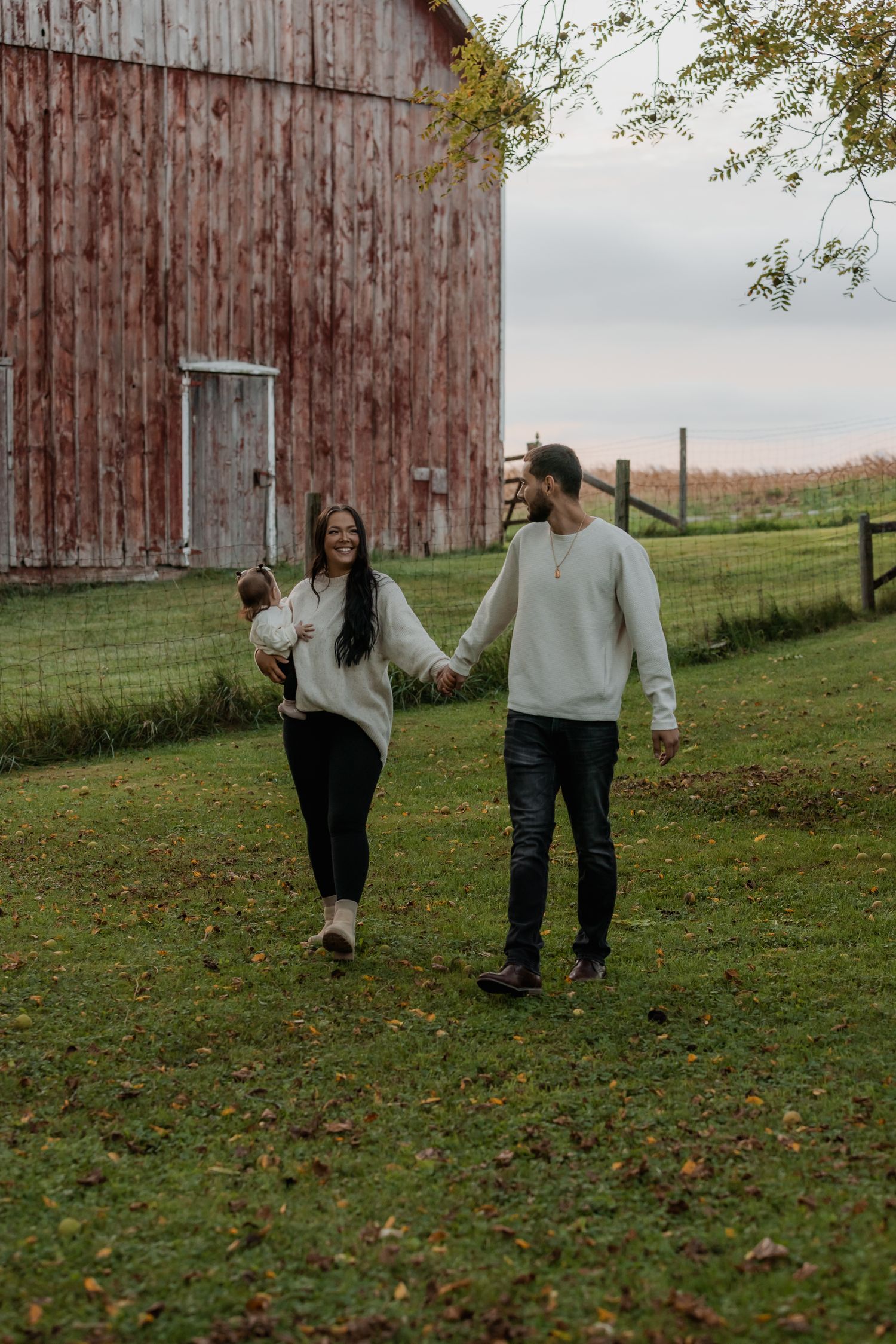 Couple walking together on grass near a rustic red barn during autumn.