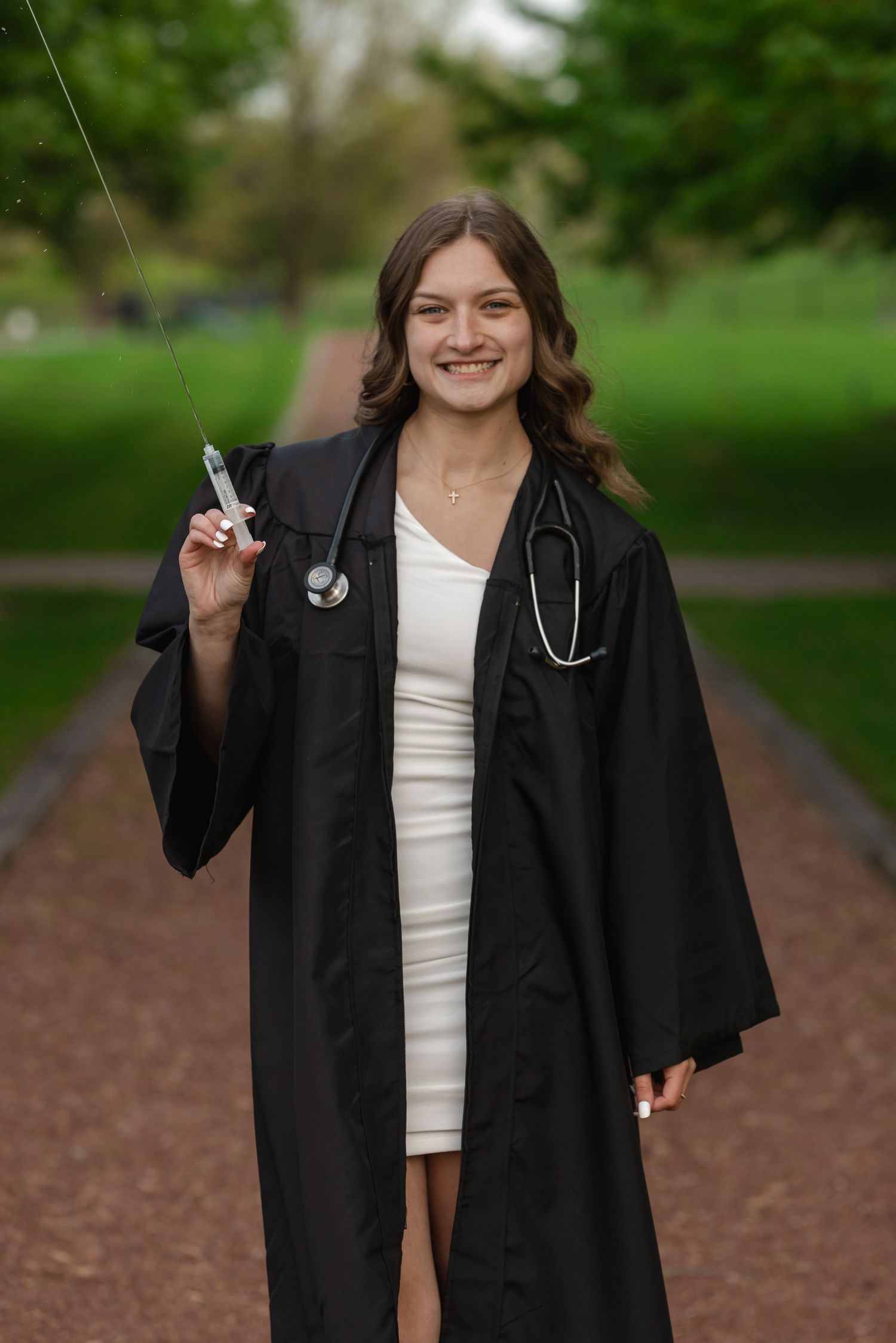 Graduate in medical attire poses with stethoscope on outdoor pathway.