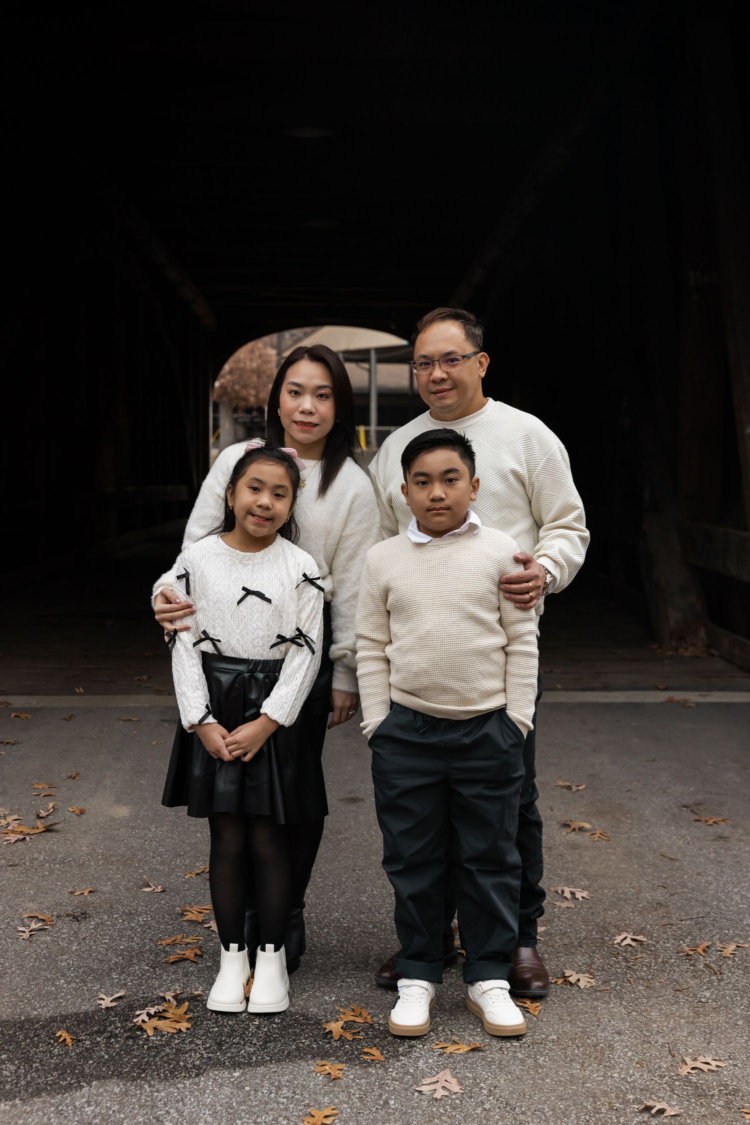 Family photo session outdoors with matching cream sweaters against dark background.