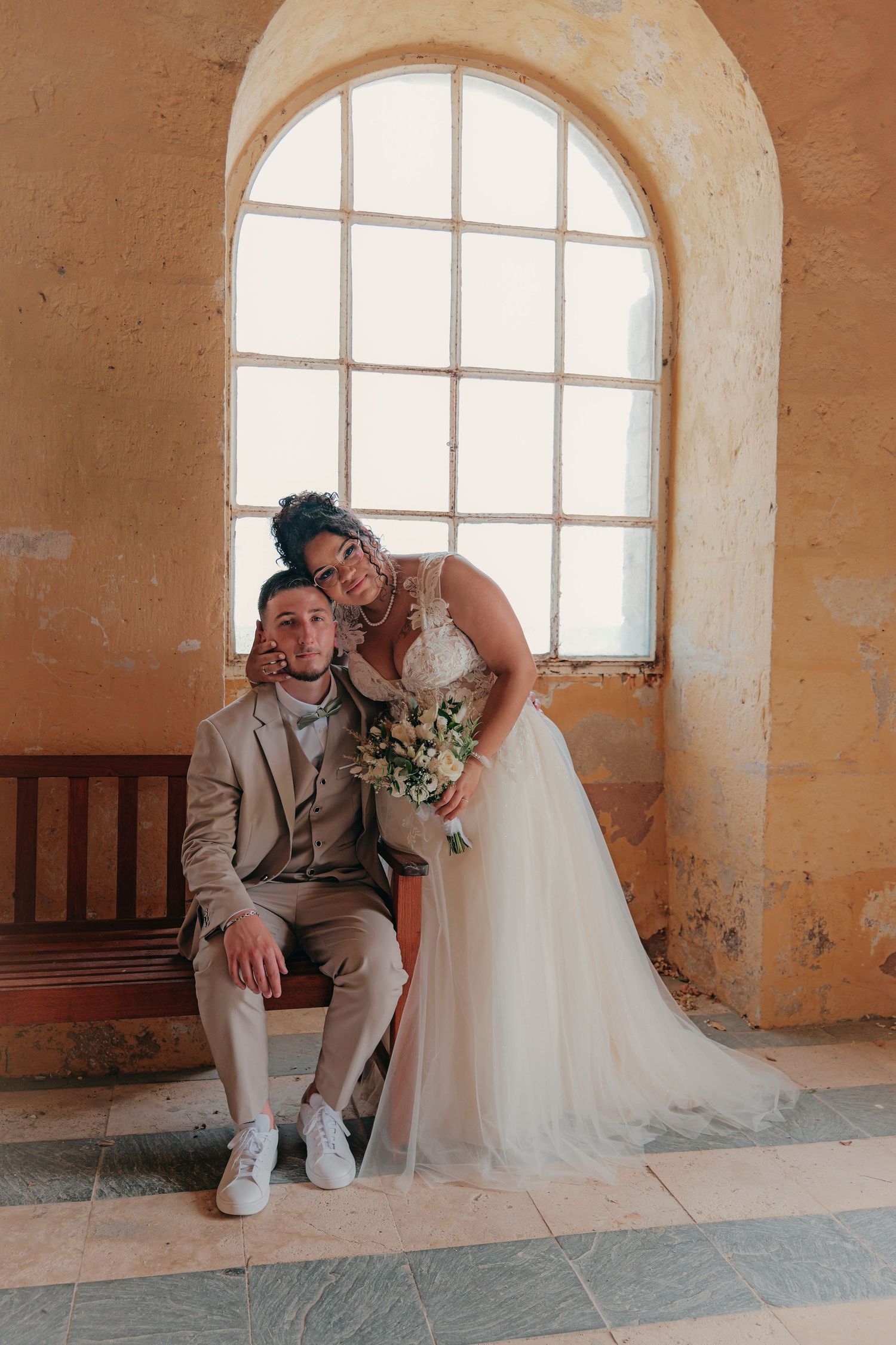 Couple de mariés devant une fenêtre.