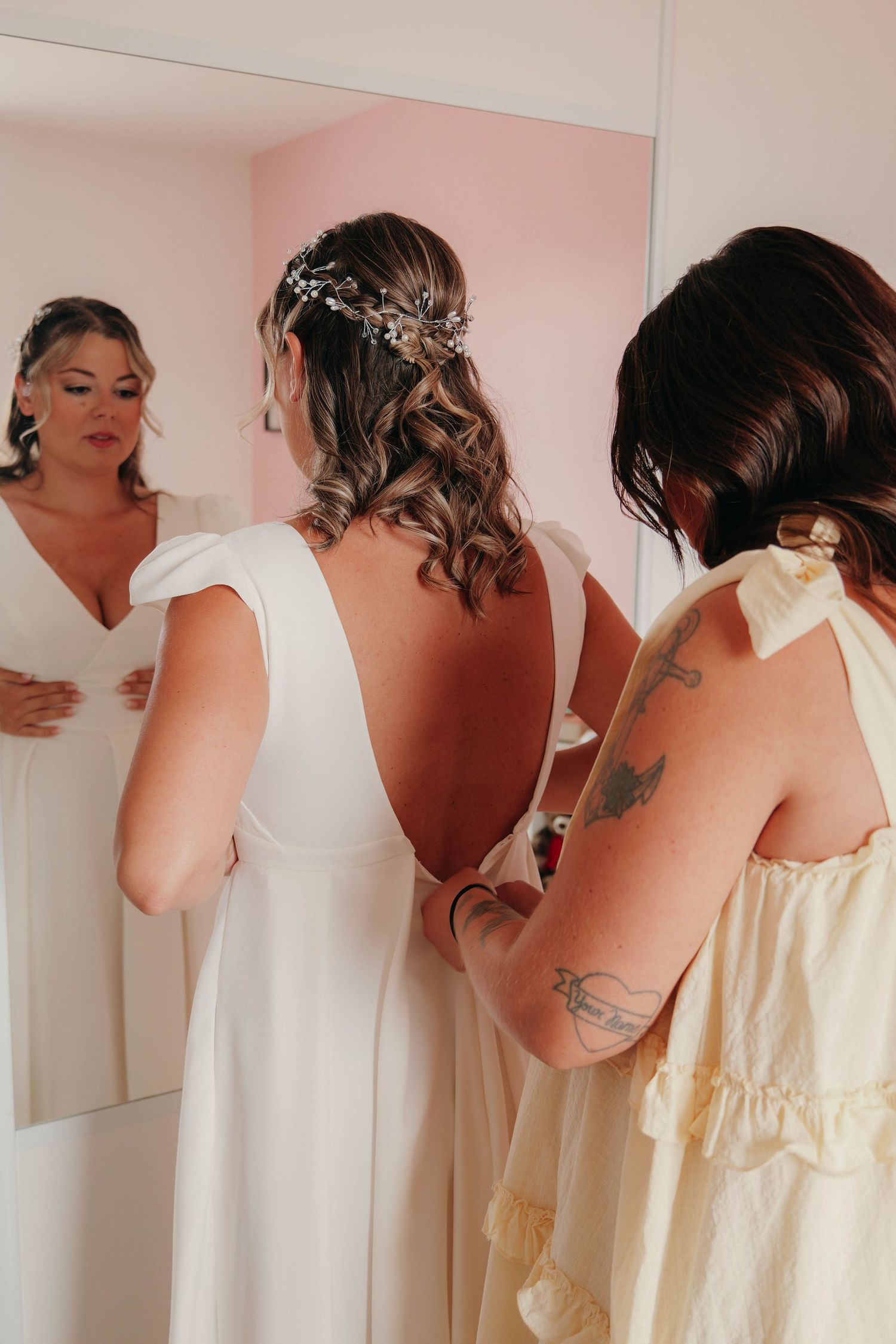 La témoin attache la robe de la mariée devant un miroir