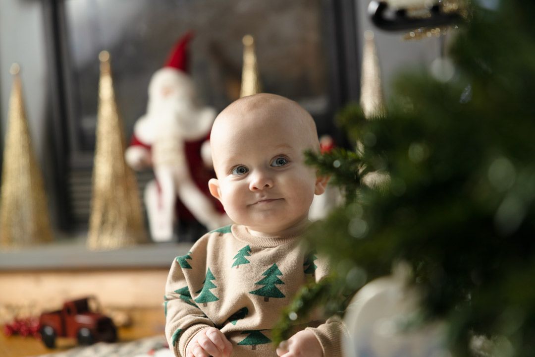 a baby sitting on the floor during a studio session admiring the Christmas tree.