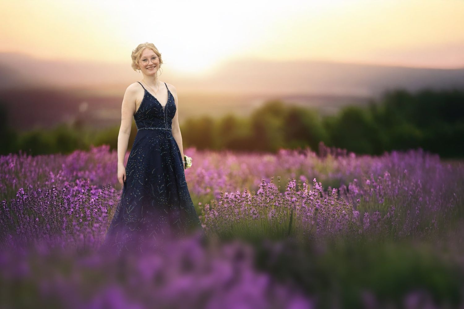 Woman in navy dress standing in purple lavender field at golden sunset.