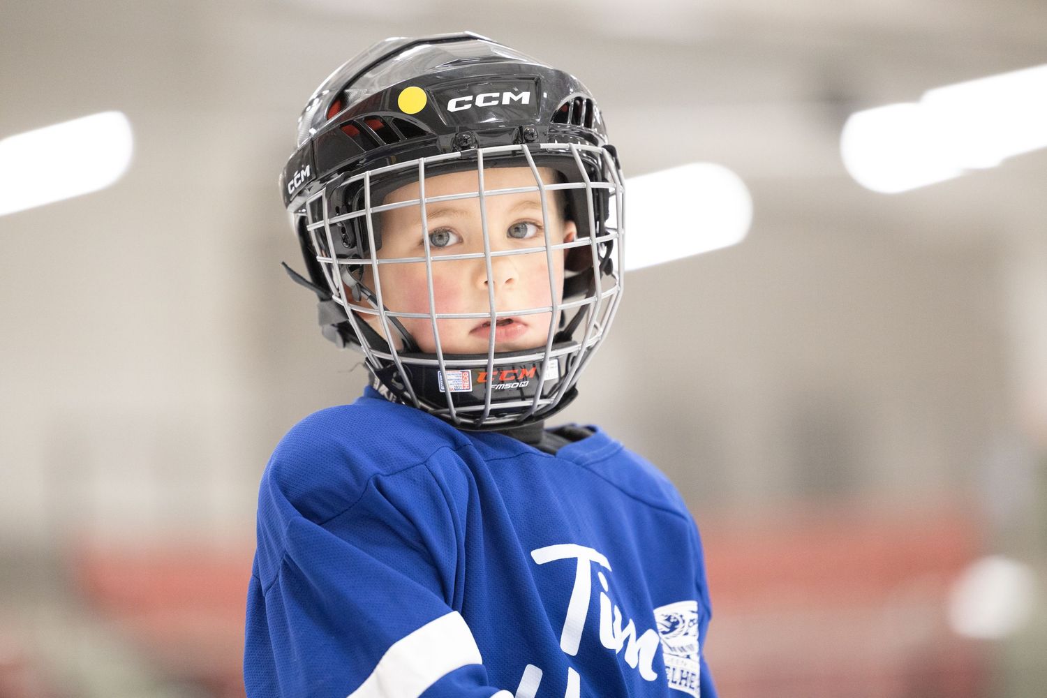 Young hockey player in blue jersey and protective gear practicing shooting drills at an indoor rink.