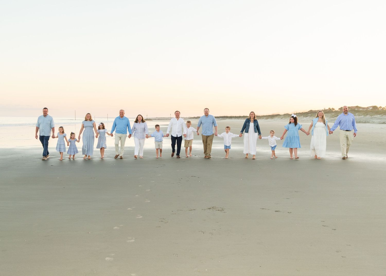 Family of 17 walking on the beach, holding hands and smiling at the camera.