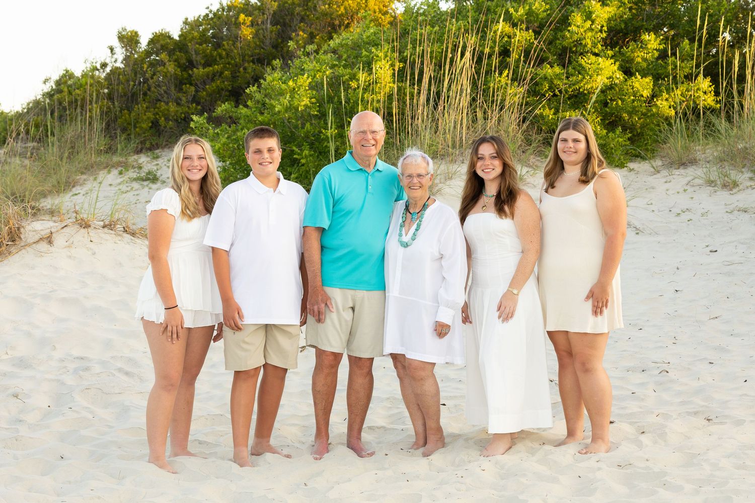 Grandparents posing with their teen grandkids standing in the dunes near the beach.