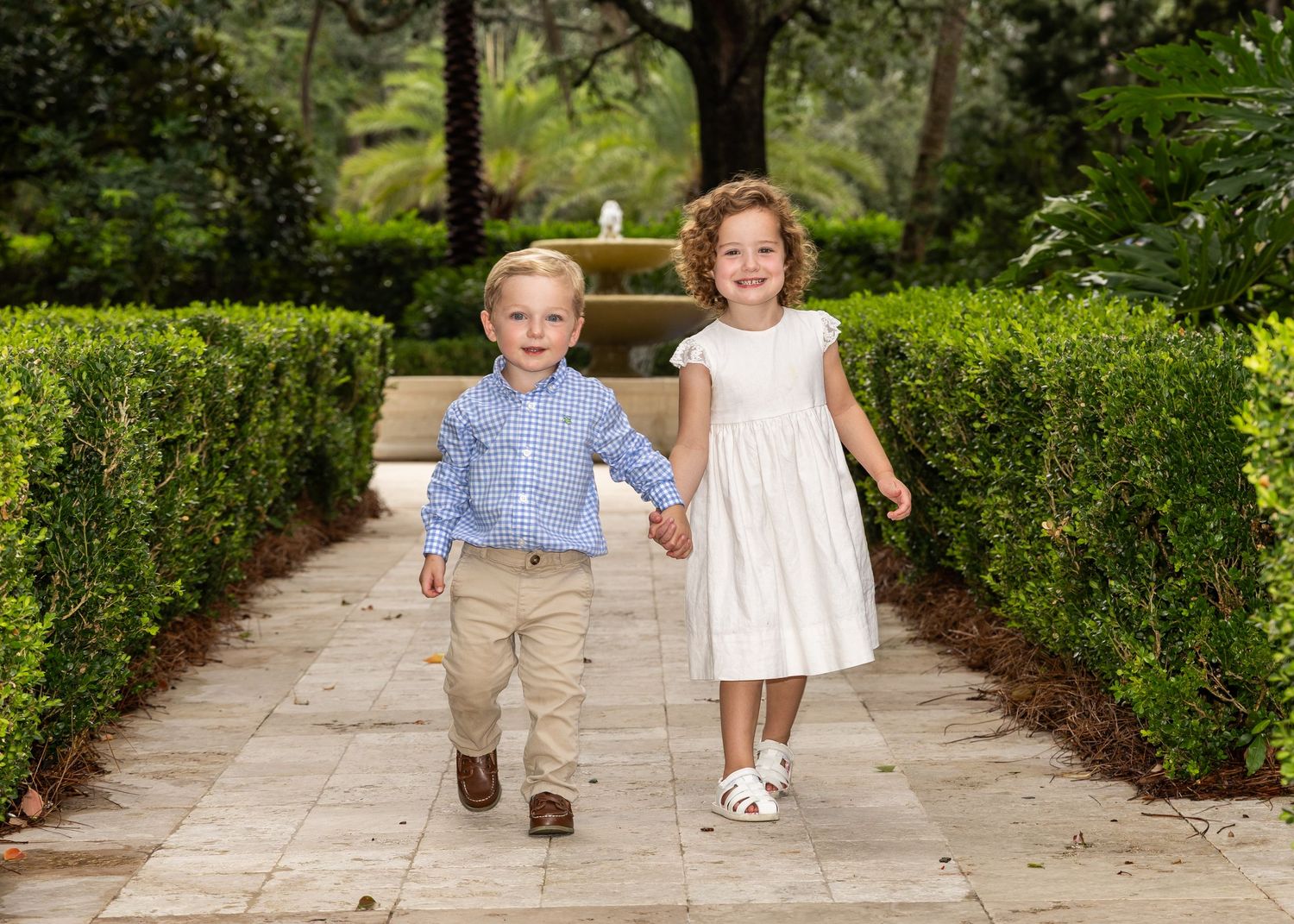 A small girl and boy (brother and sister) are walking and smiling towards the camera.