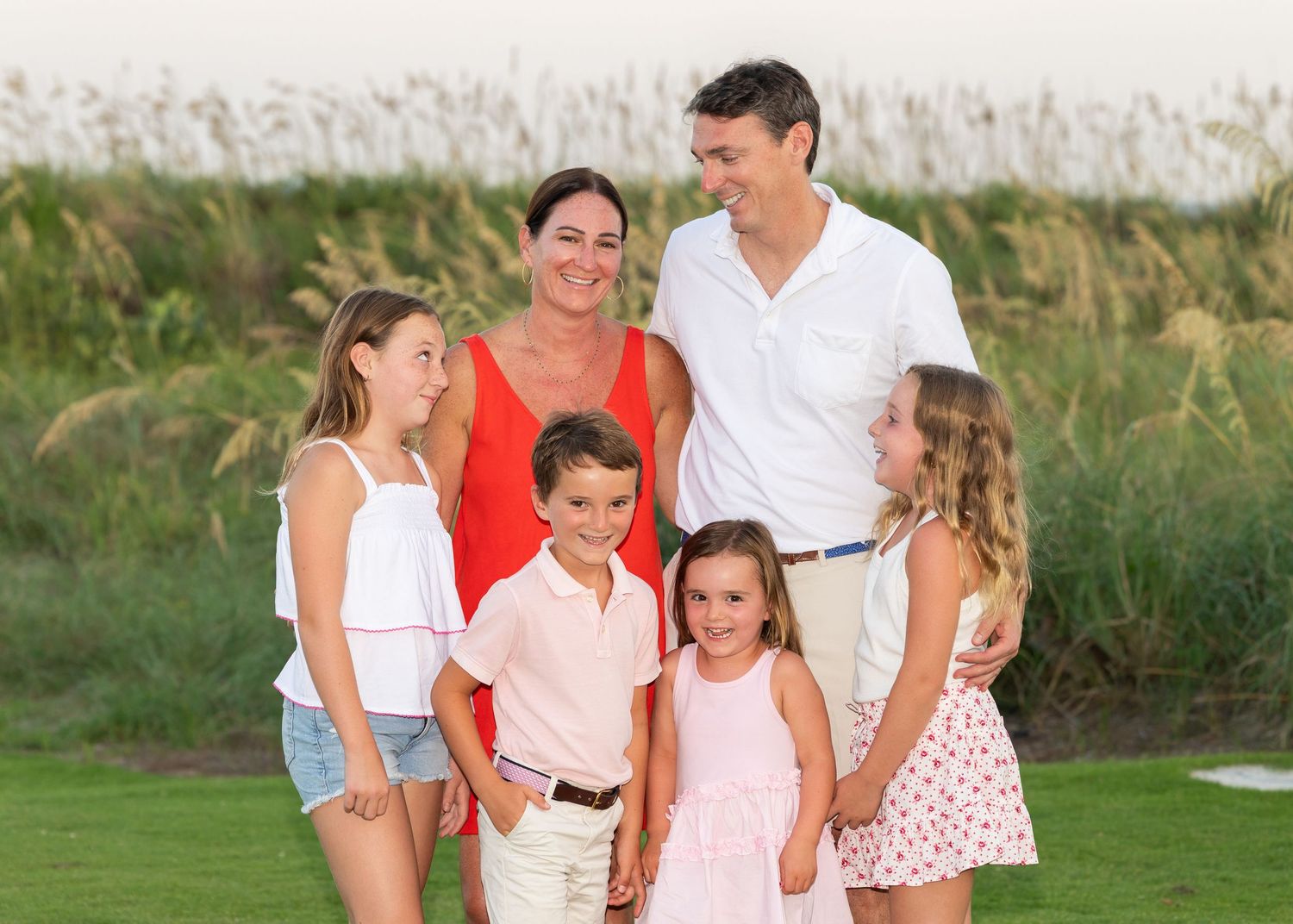 A family of 6 laughing and looking at each other in front of dunes at the beach