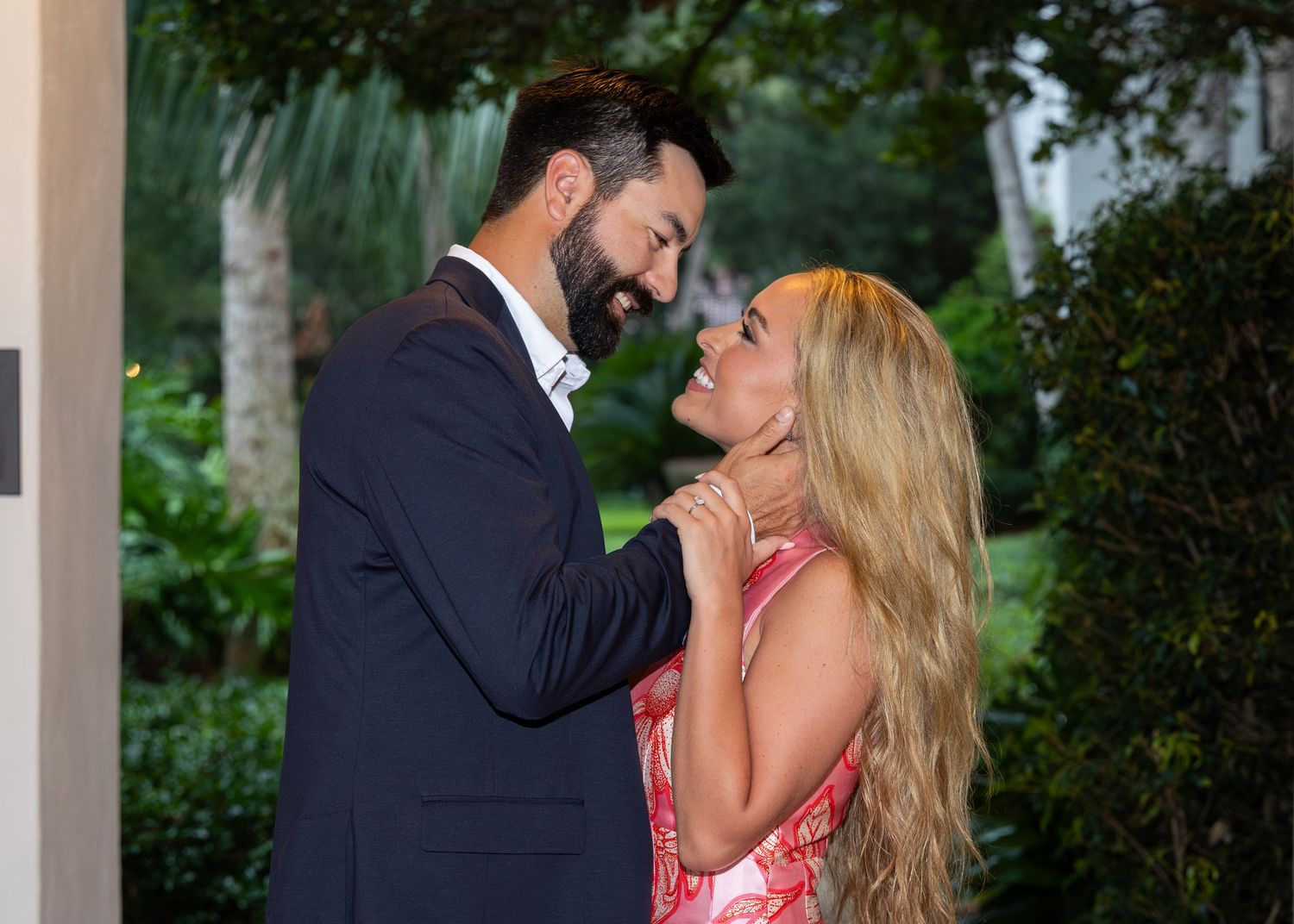 A close up of a couple looking into each other's eyes and smiling. Her hand is resting on his, showing off her engagement ring.