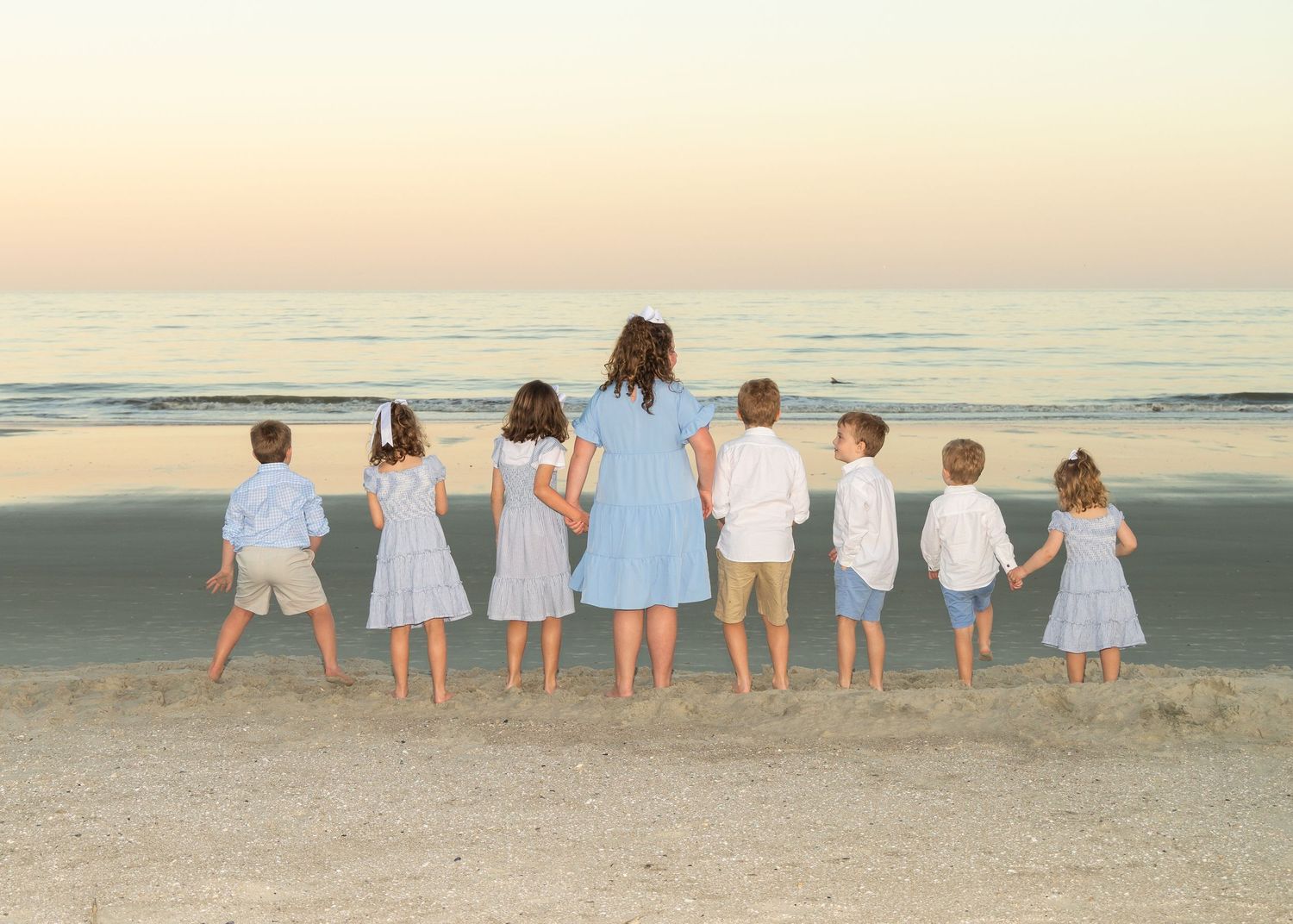 Kids (cousins) with backs to the camera are looking out at the water where a dolphin can be seen in the surf