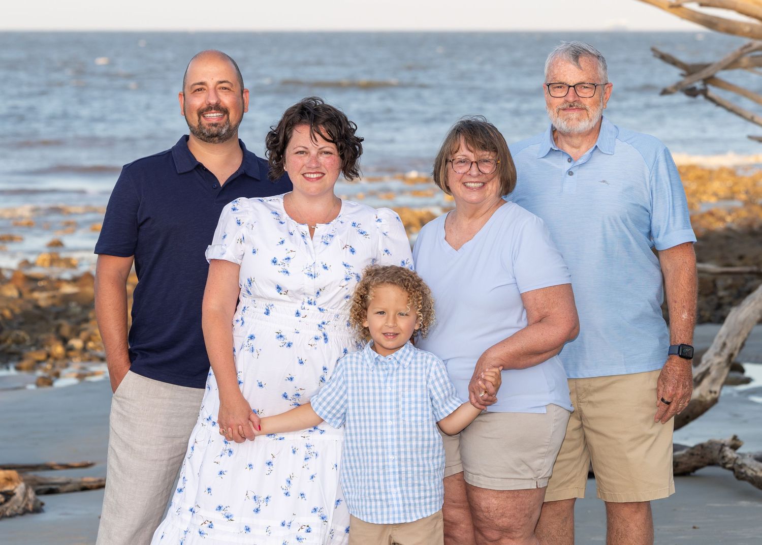 A family of 5, posed and smiling at the camera at Driftwood Beach