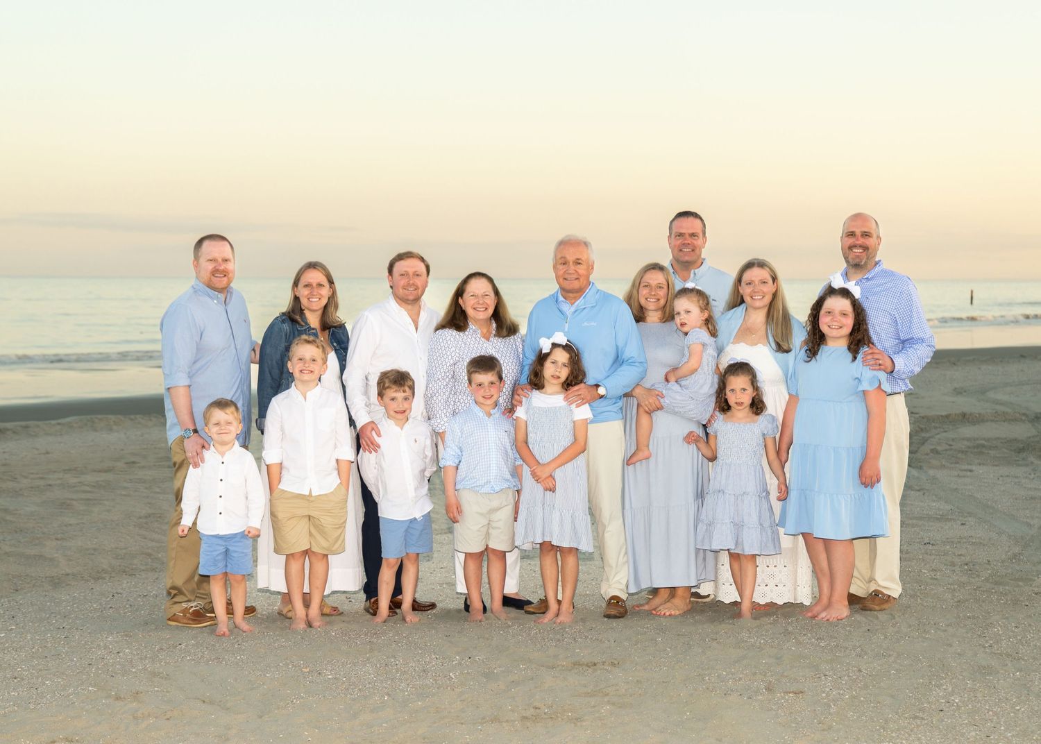 A family of 17 standing on a sunset beach, posed and smiling at the camera.