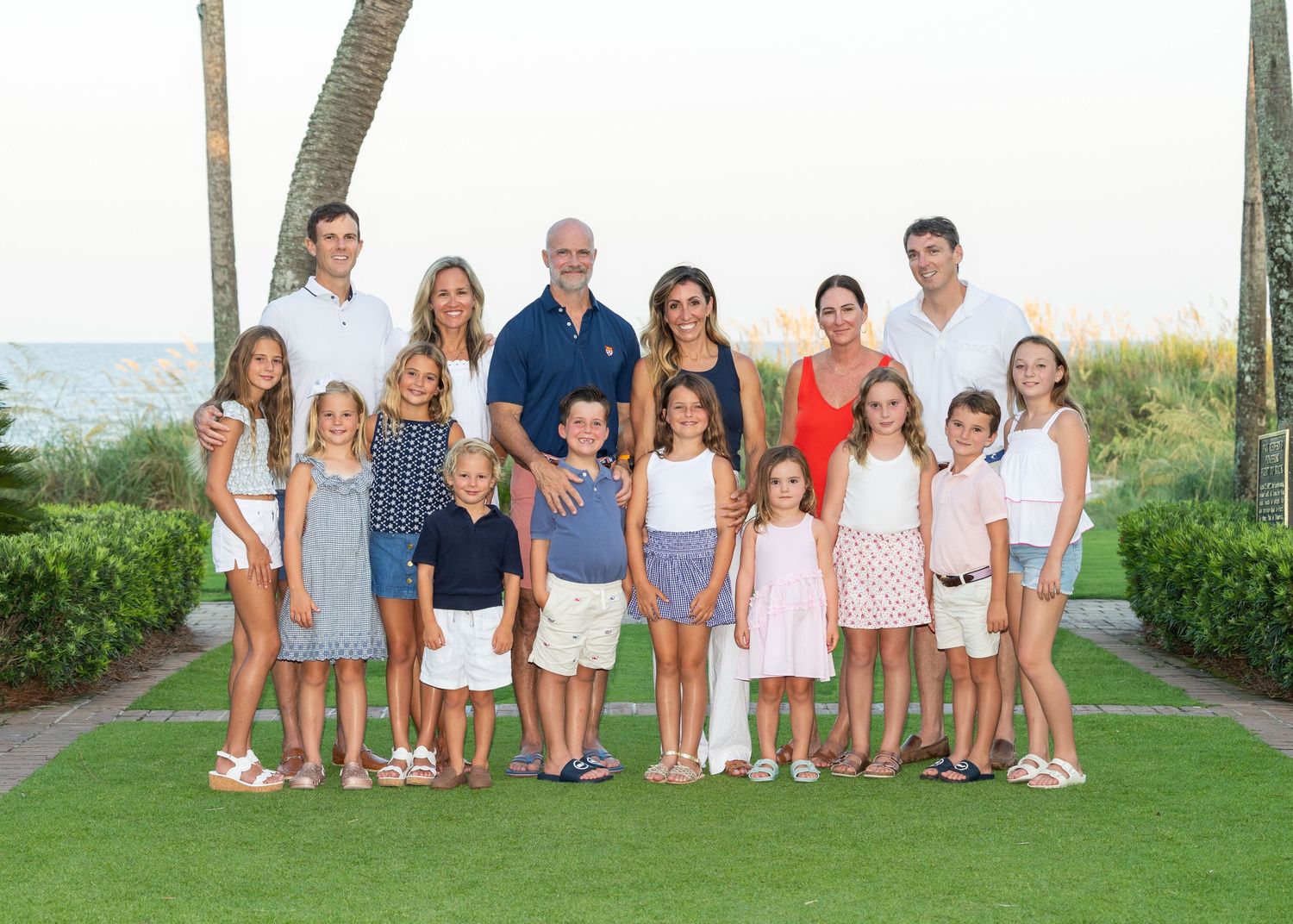 A group of 16 standing in front of the ocean, smiling and posed looking at the camera.