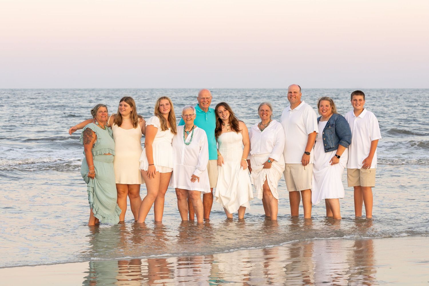 A family of 10 standing ankle deep in the water, posing and smiling at the camera.