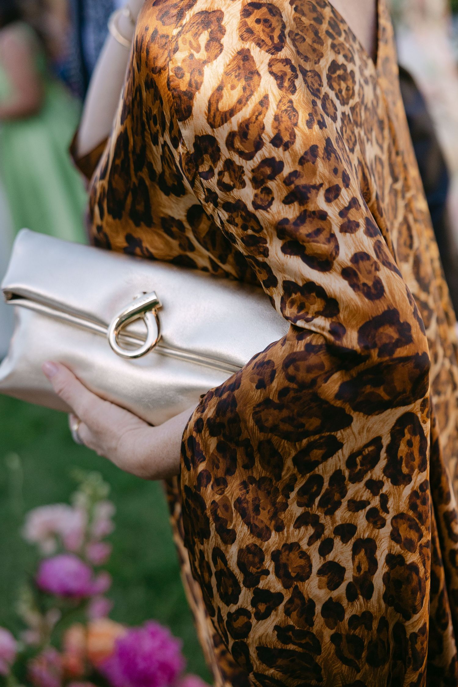 Guest in leopard print dress holding gold clutch purse at outdoor wedding event.