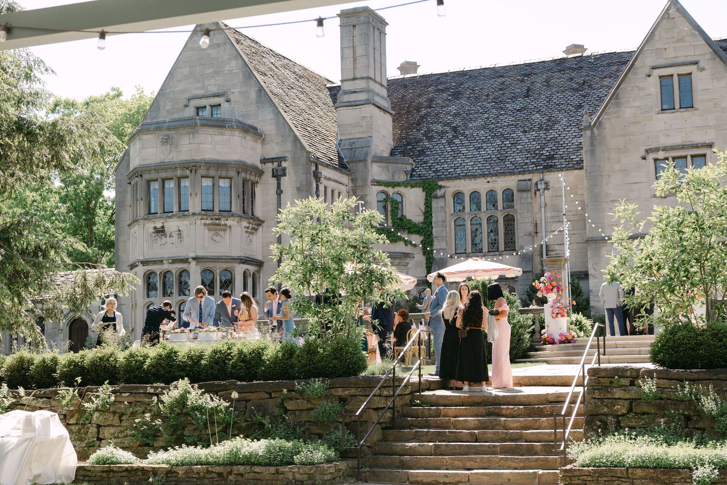 Guests mingling outside a grand stone manor house venue during an outdoor wedding cocktail hour.