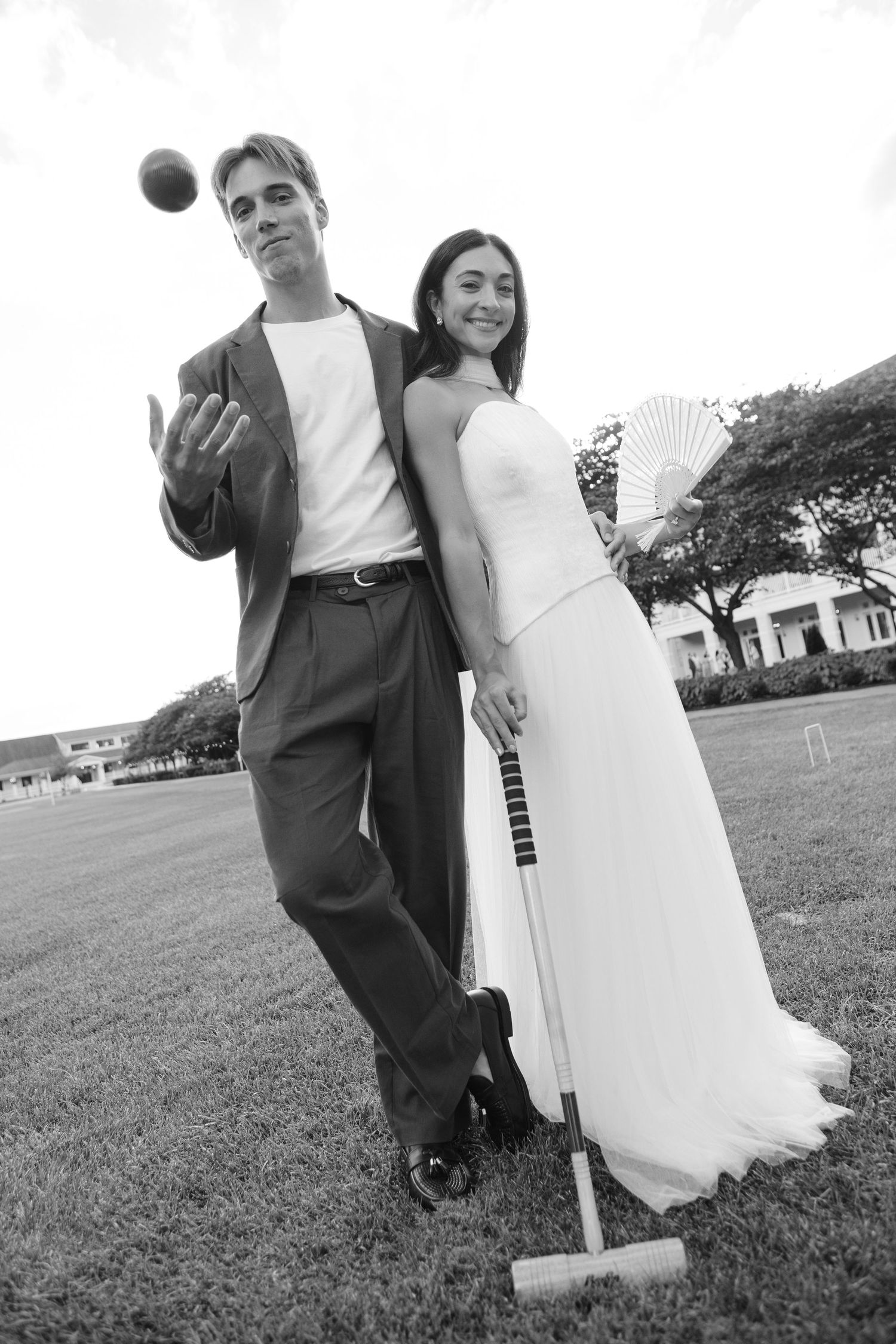 Black and white photo of a bride and groom playing croquet on a lawn, woman in white gown holding mallet.