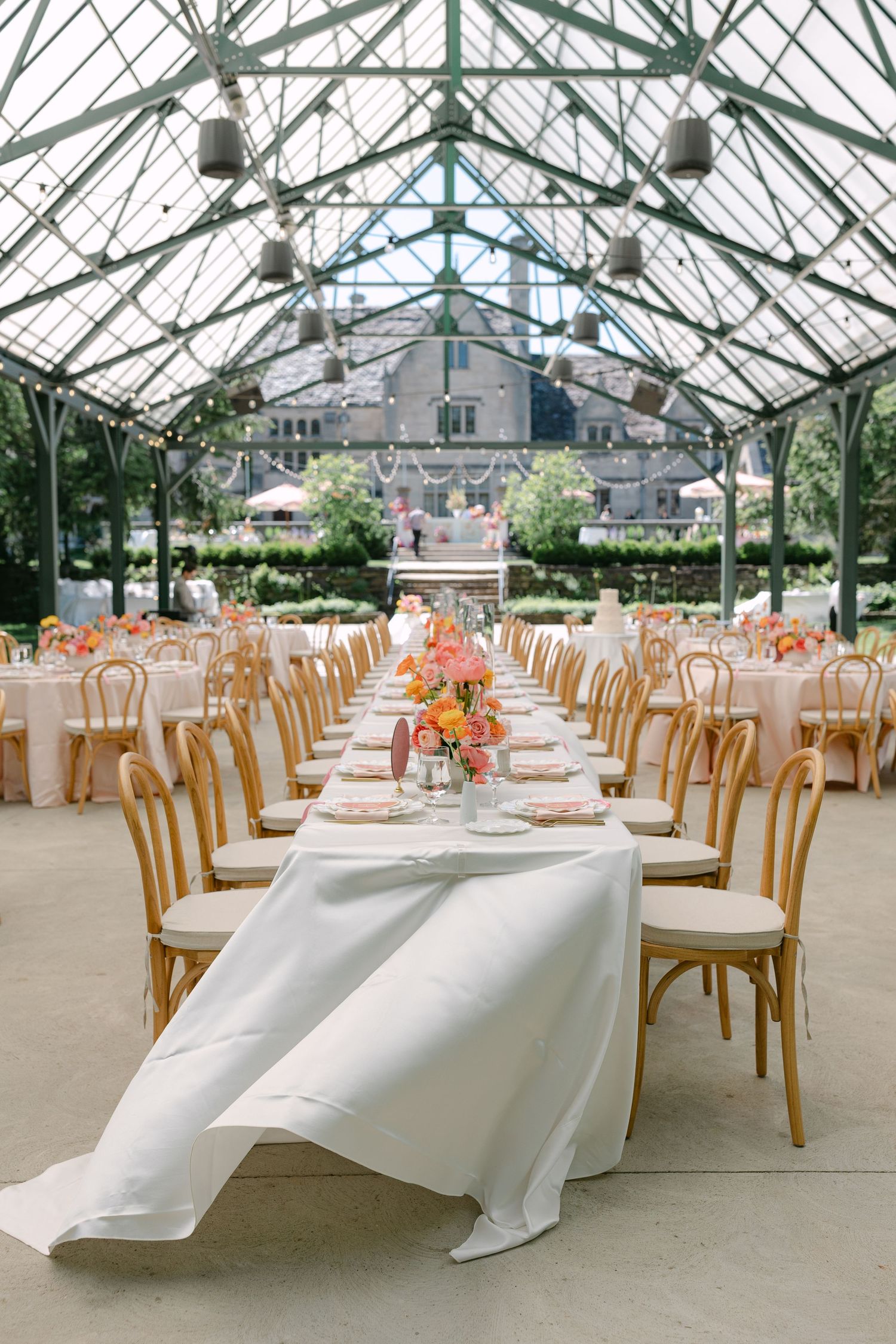 Elegant greenhouse wedding reception featuring long head table with white linen and colorful floral arrangements.