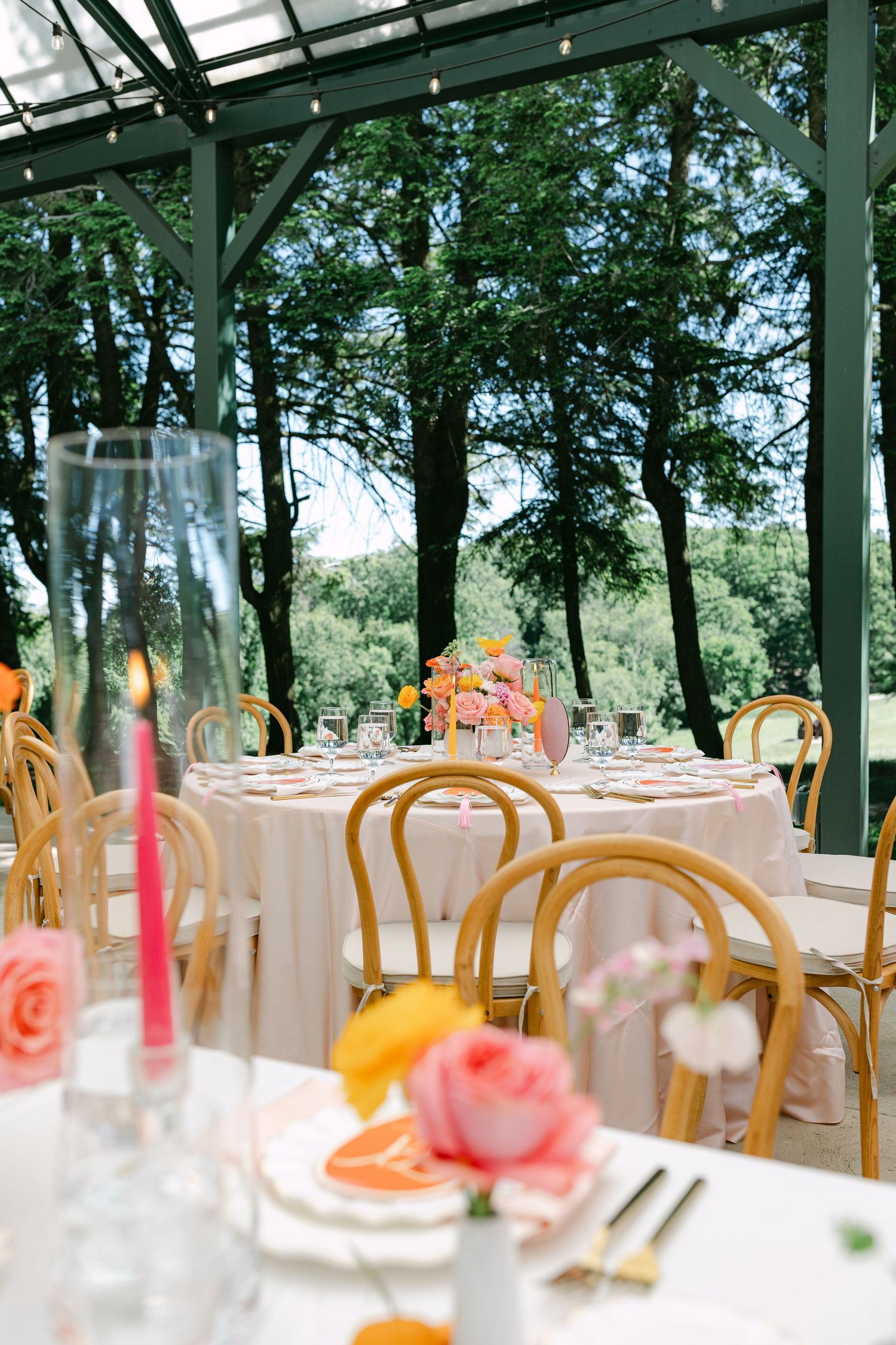 Romantic greenhouse wedding reception with bentwood chairs, blush tablecloths, pink floral centerpieces, and tall candles.