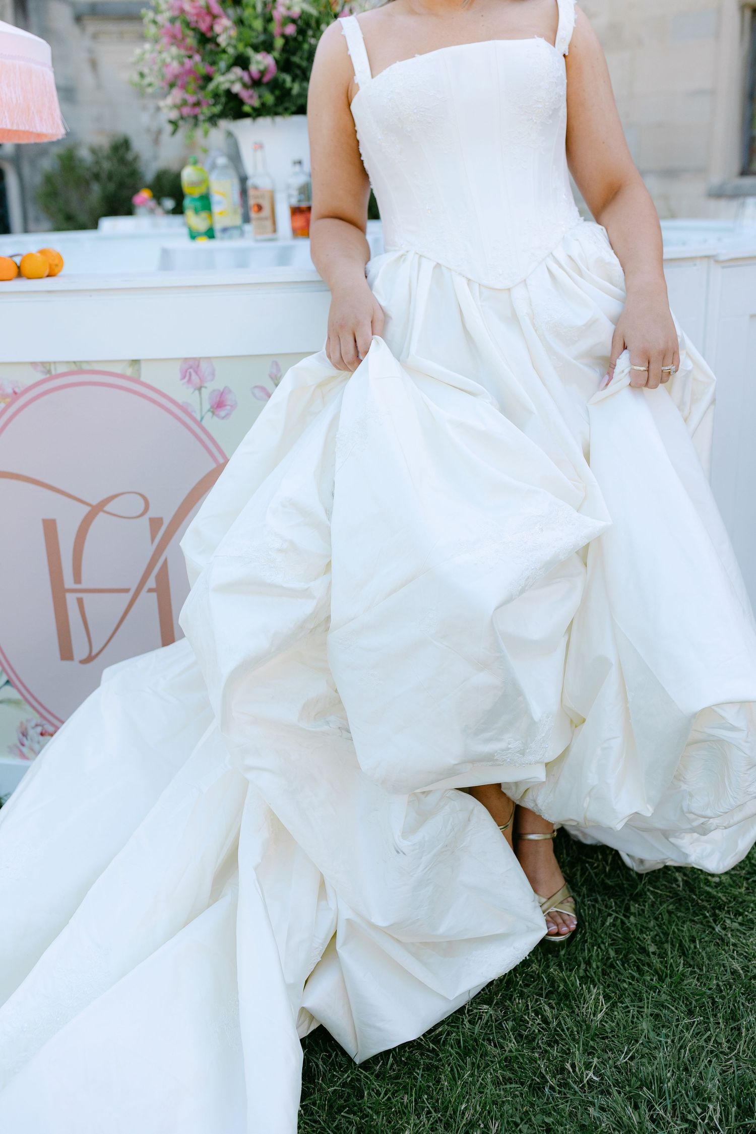 Bride in a voluminous white ball gown with structured bodice and dramatic skirt standing outdoors at wedding reception.