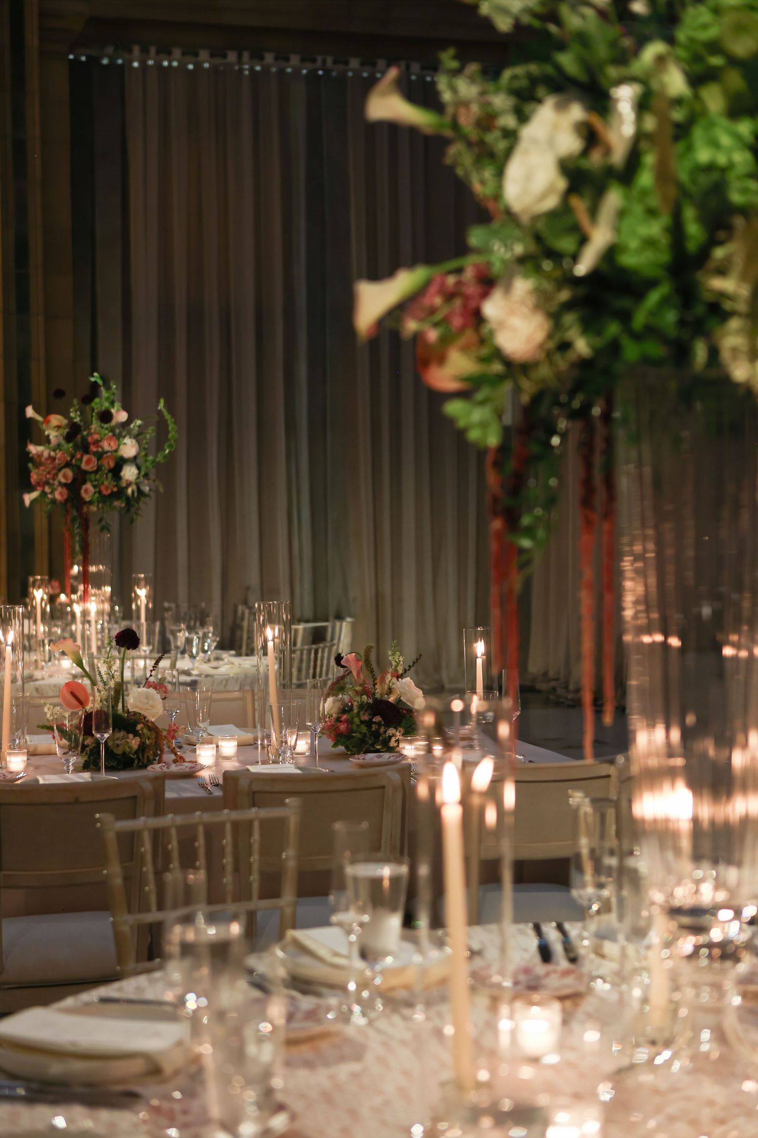 Dimly lit wedding reception with candlelit tables, gold chiavari chairs, and tall floral centerpieces.