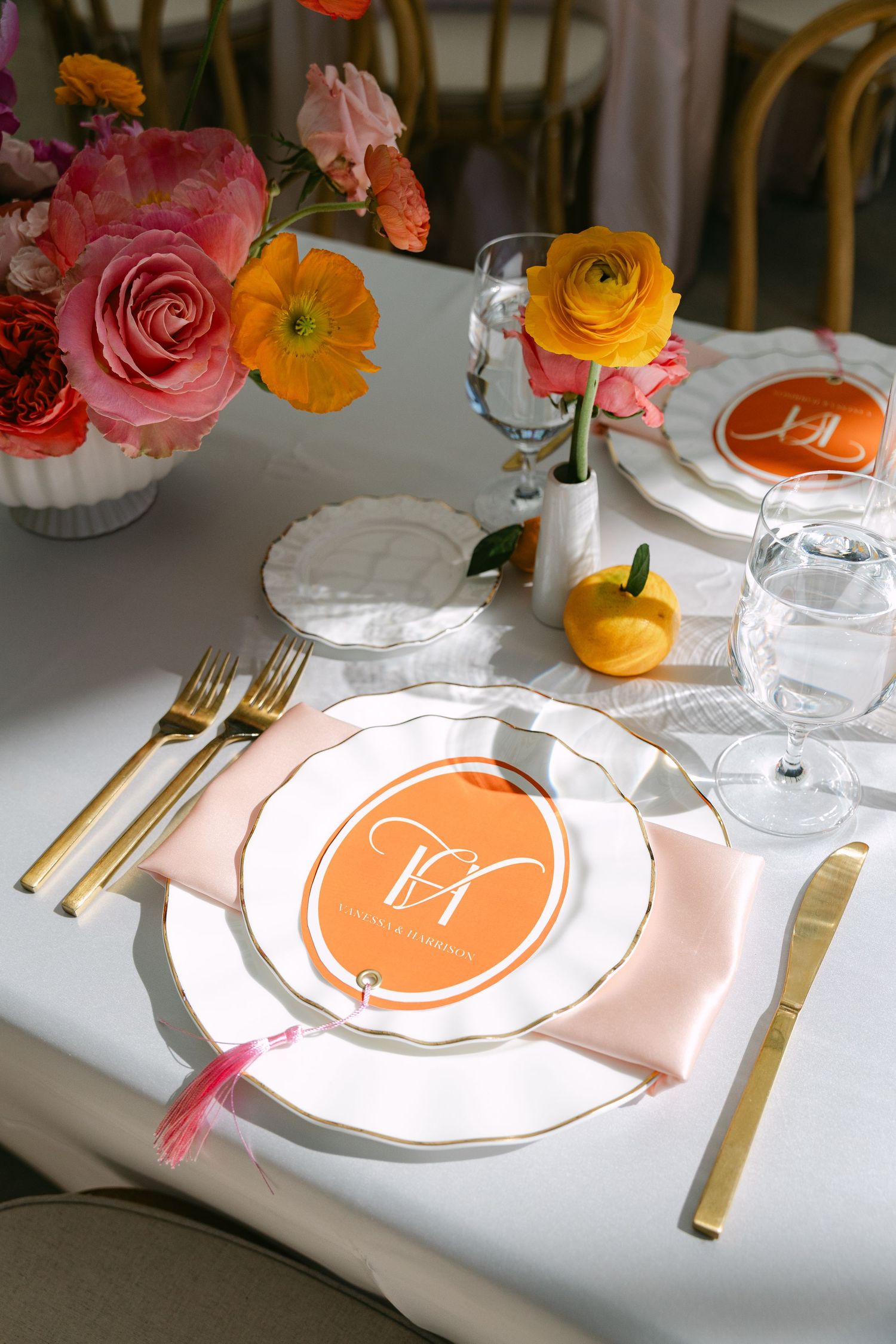 Elegant wedding place setting with orange monogram menu card, gold flatware, and colorful floral centerpiece.