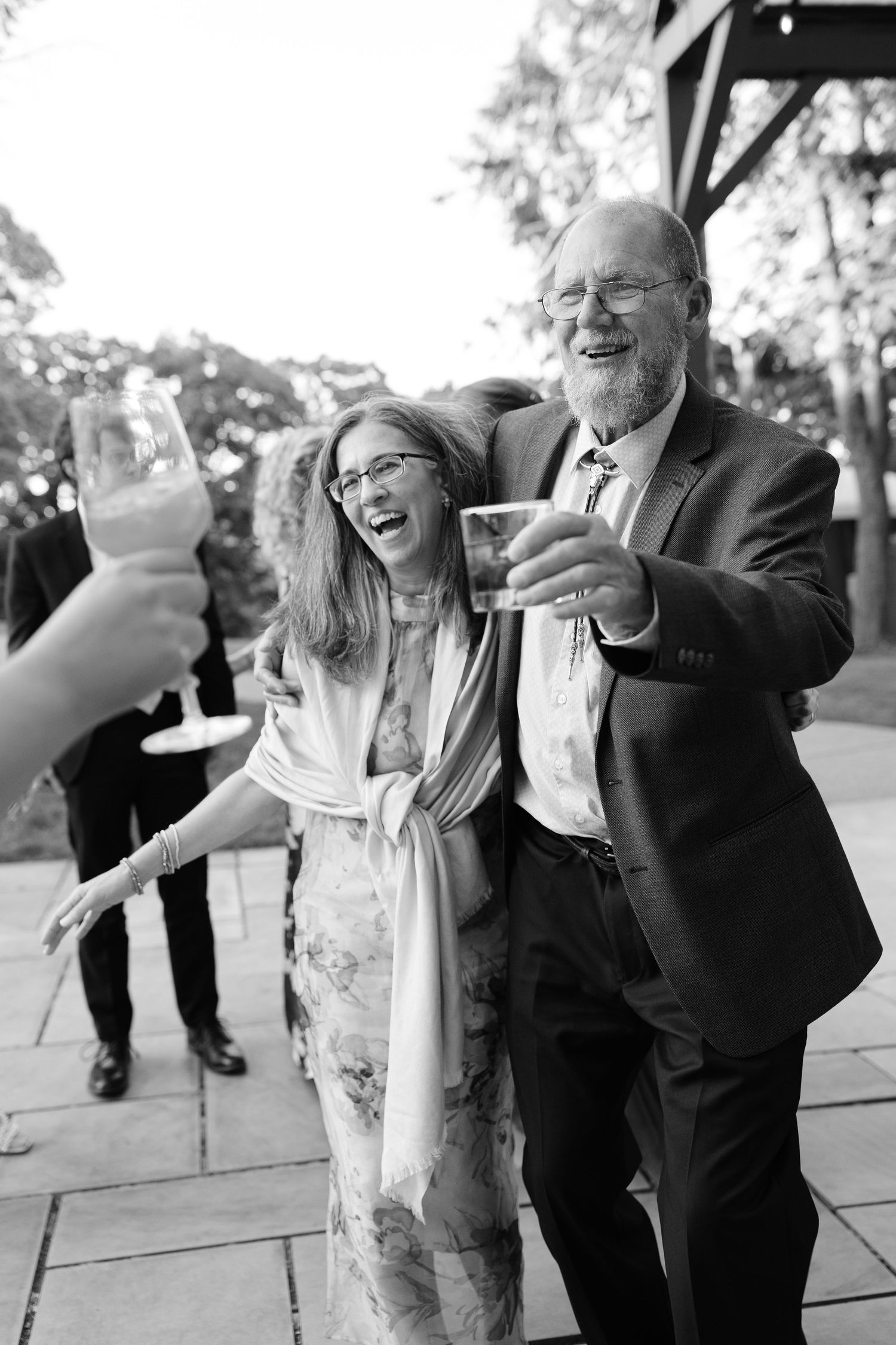 Couple laughing and toasting with champagne glasses at outdoor wedding reception in black and white.